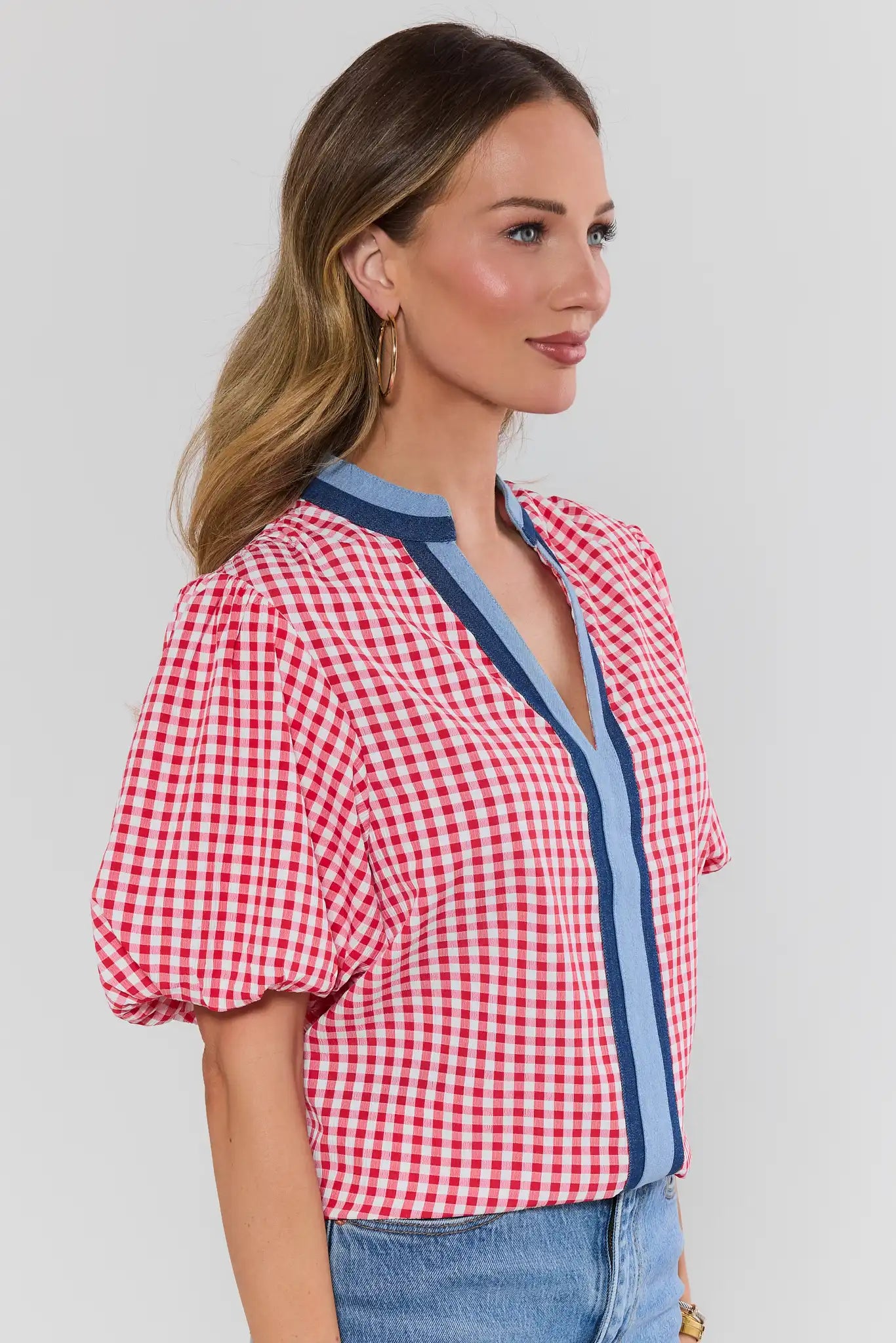 Woman wearing a red and white checkered blouse with blue accents on a plain background side