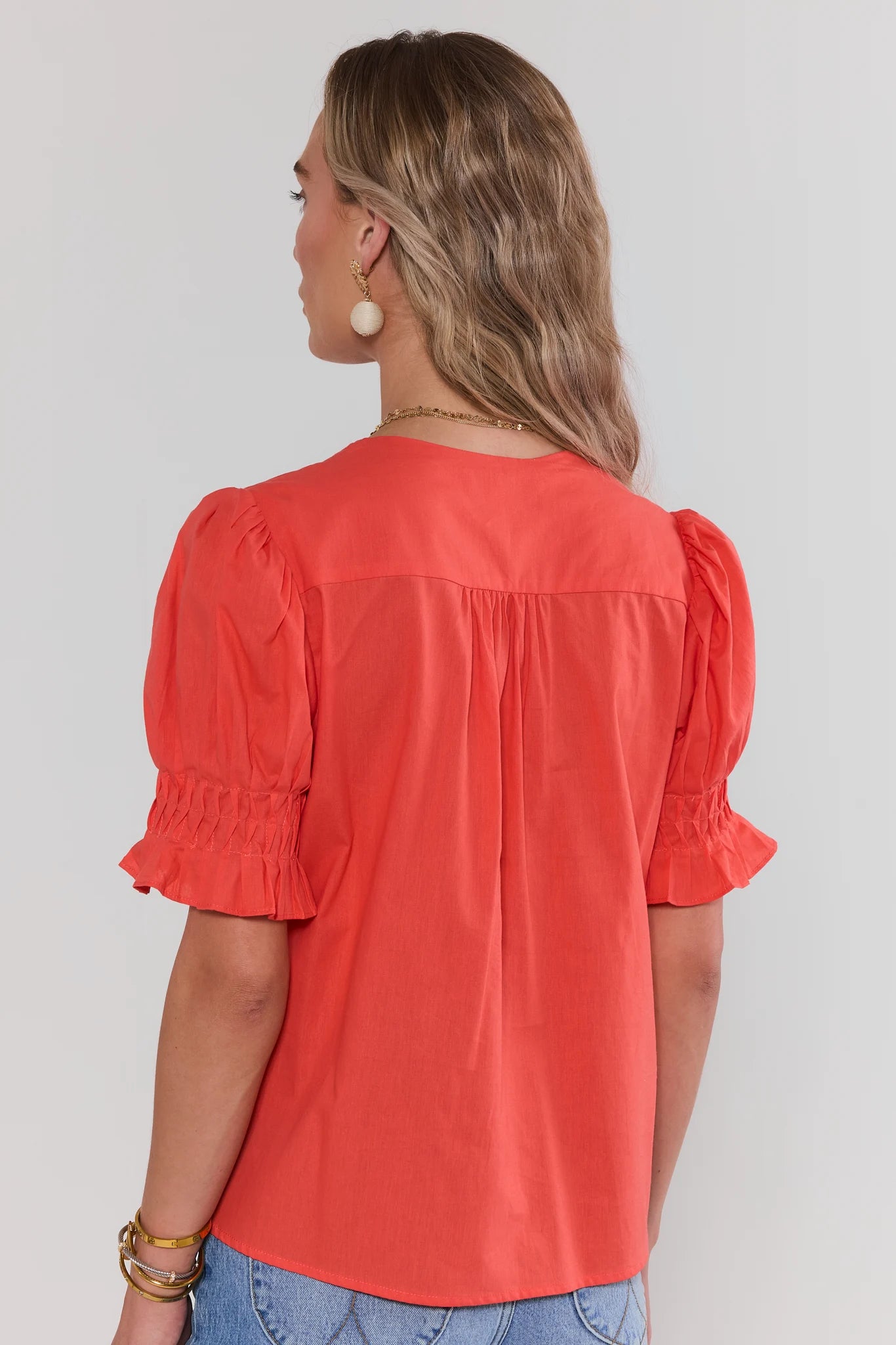 Woman standing wearing a red blouse with puff sleeves against a plain background