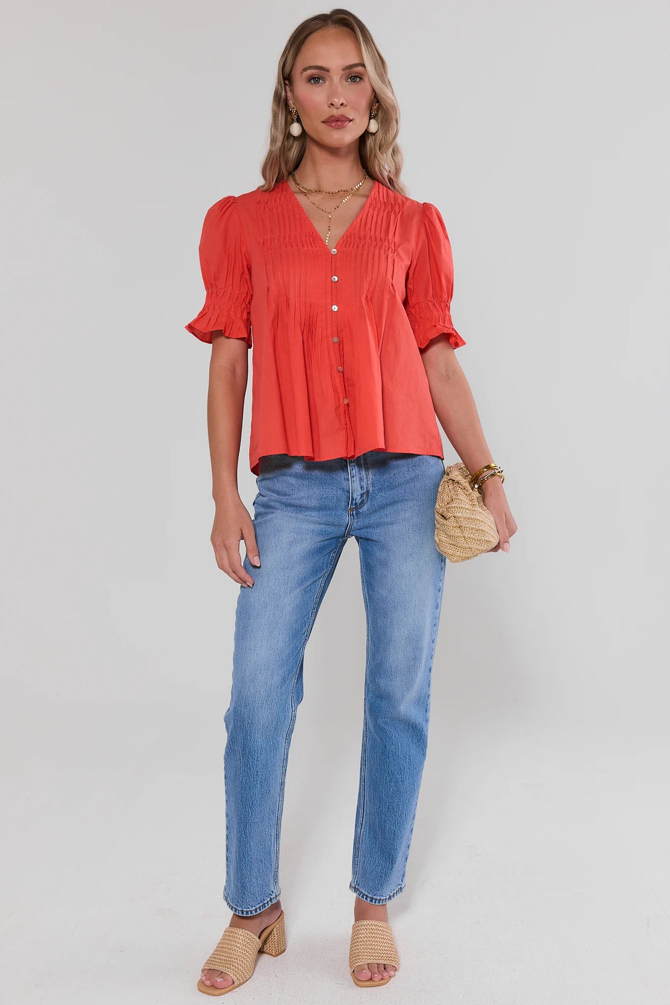 Woman wearing a coral blouse and blue jeans on a white background standing