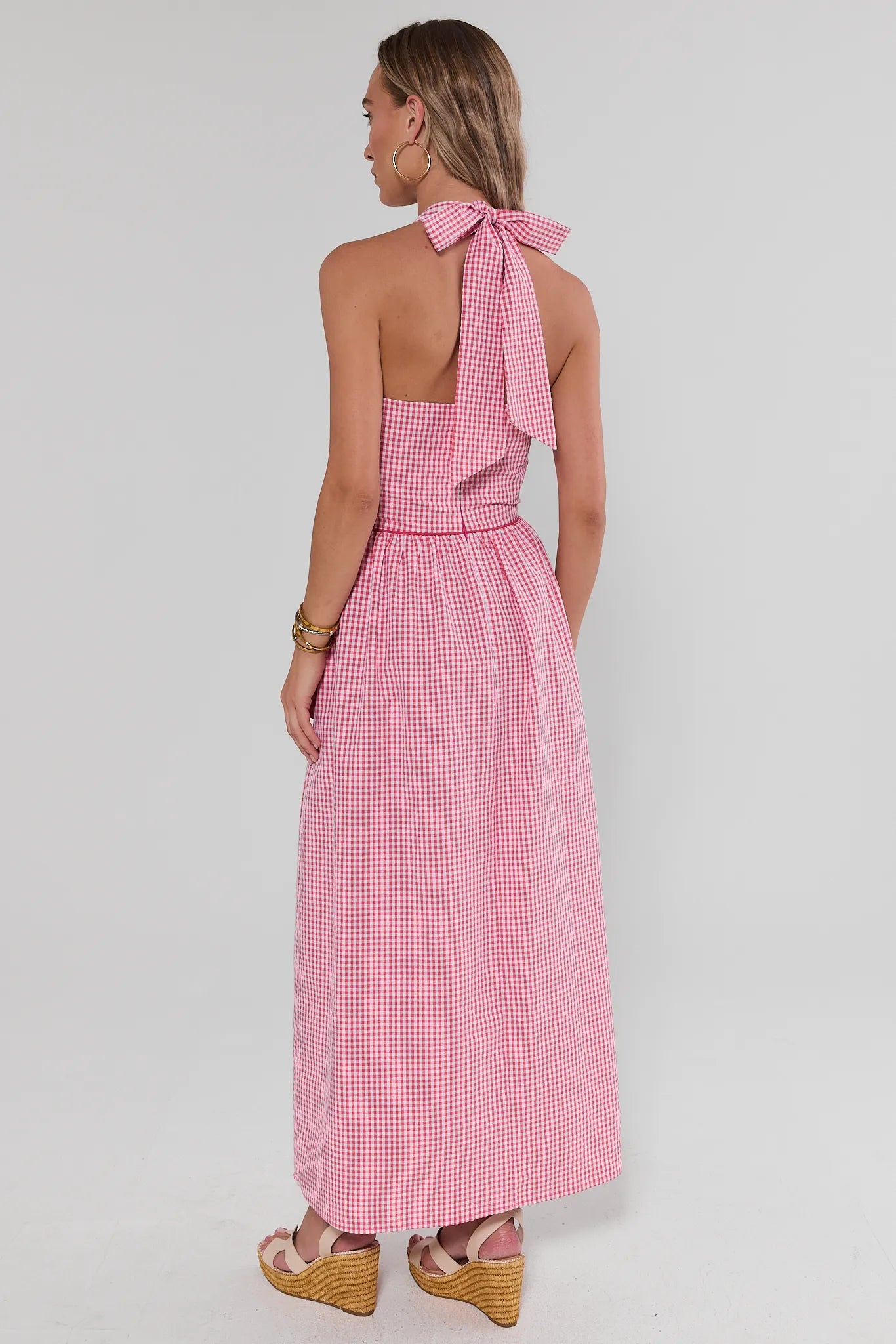 Woman standing wearing a pink gingham dress with a bow detail on a white background