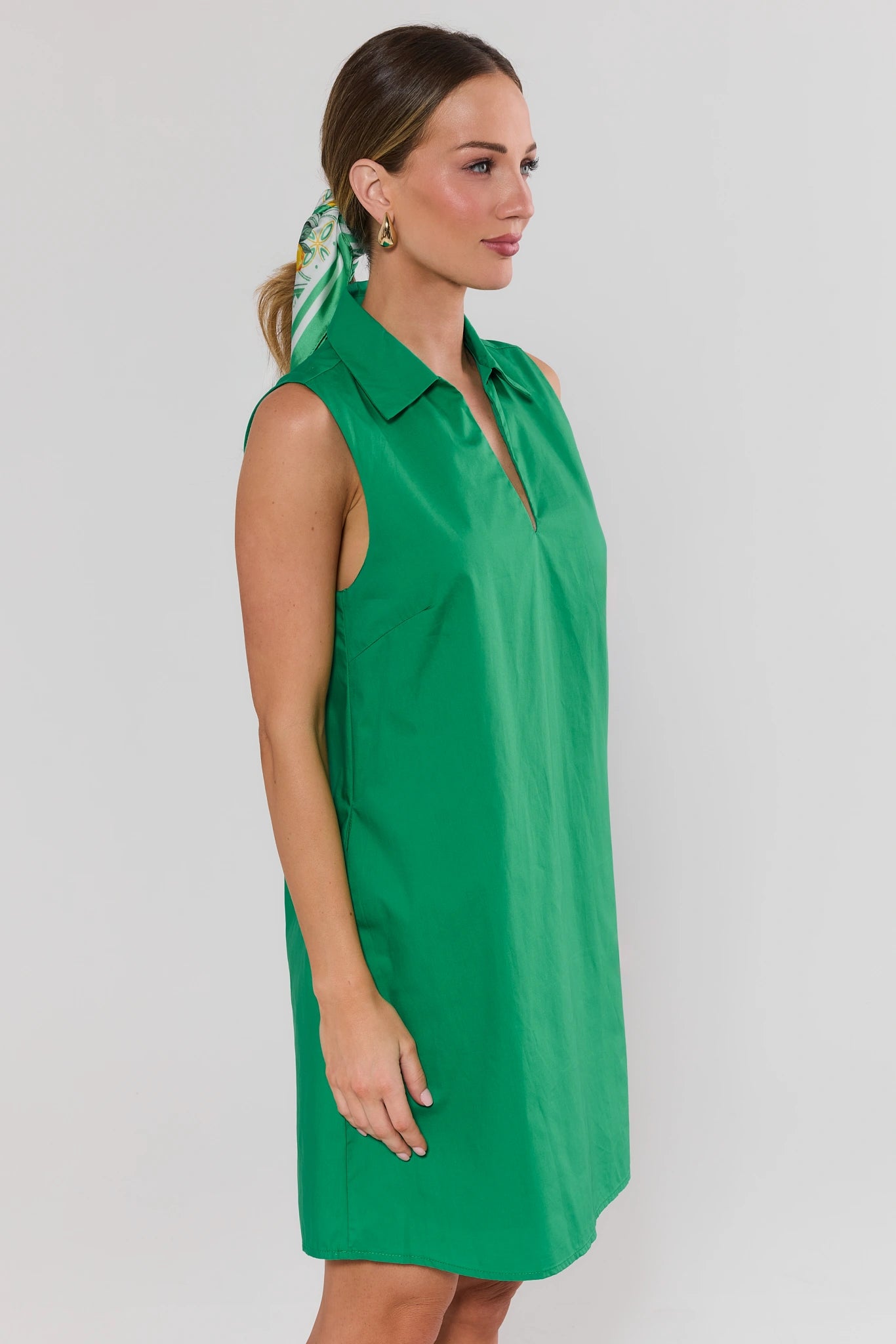 Woman wearing a green sleeveless dress with a plain background side