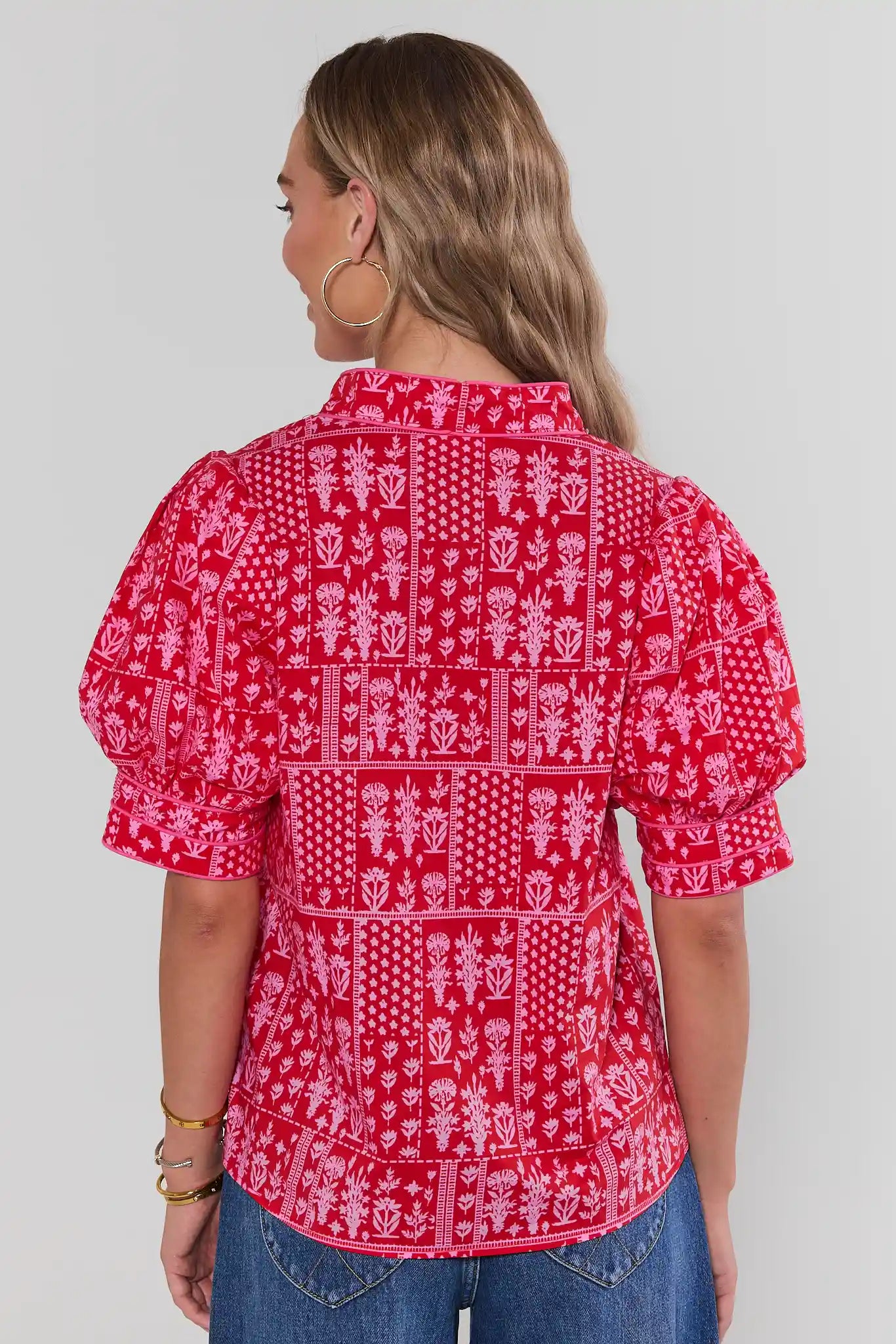 Woman wearing a red patterned blouse with blue jeans on a white background standing