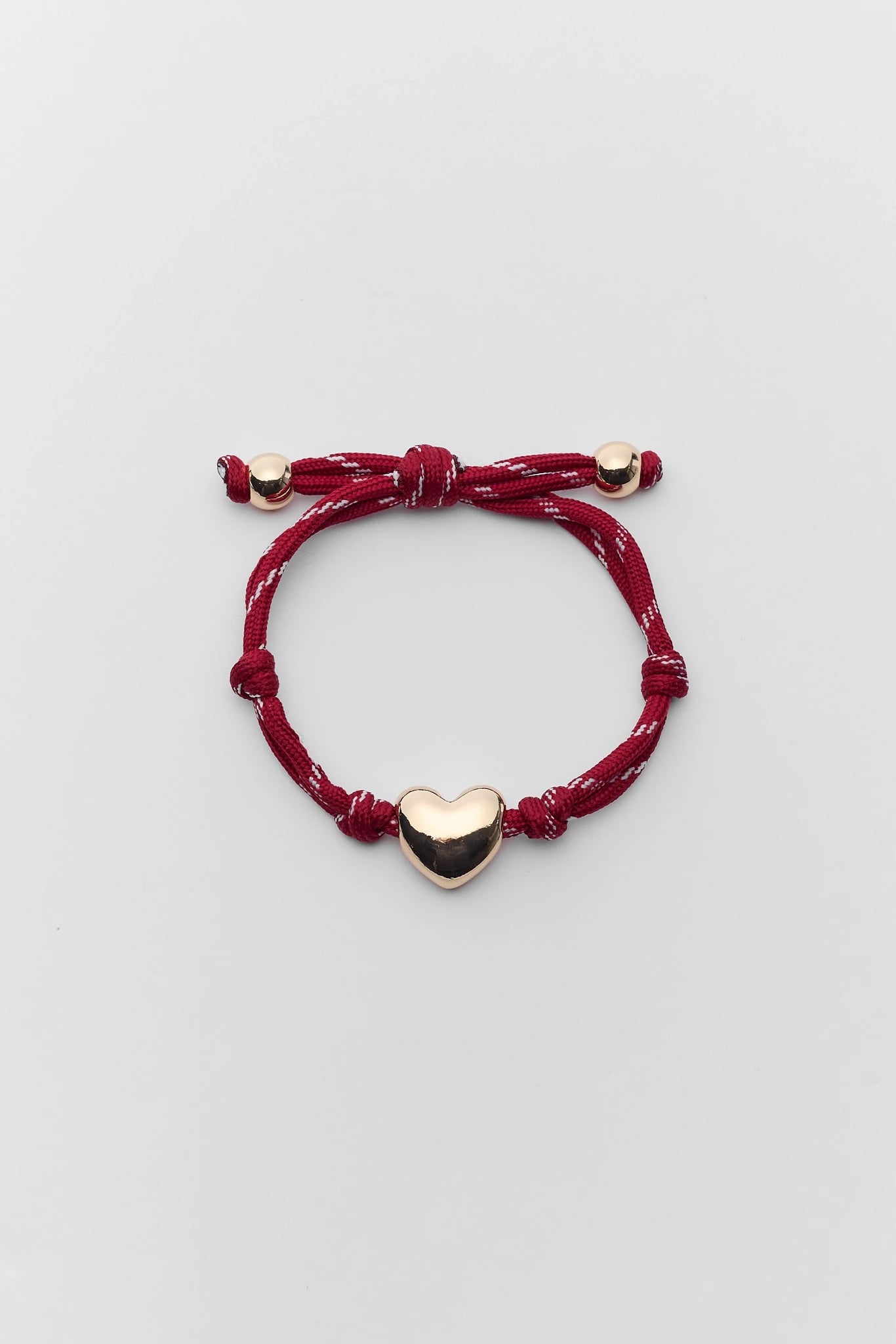 Red bracelet with a heart-shaped charm on a light gray background