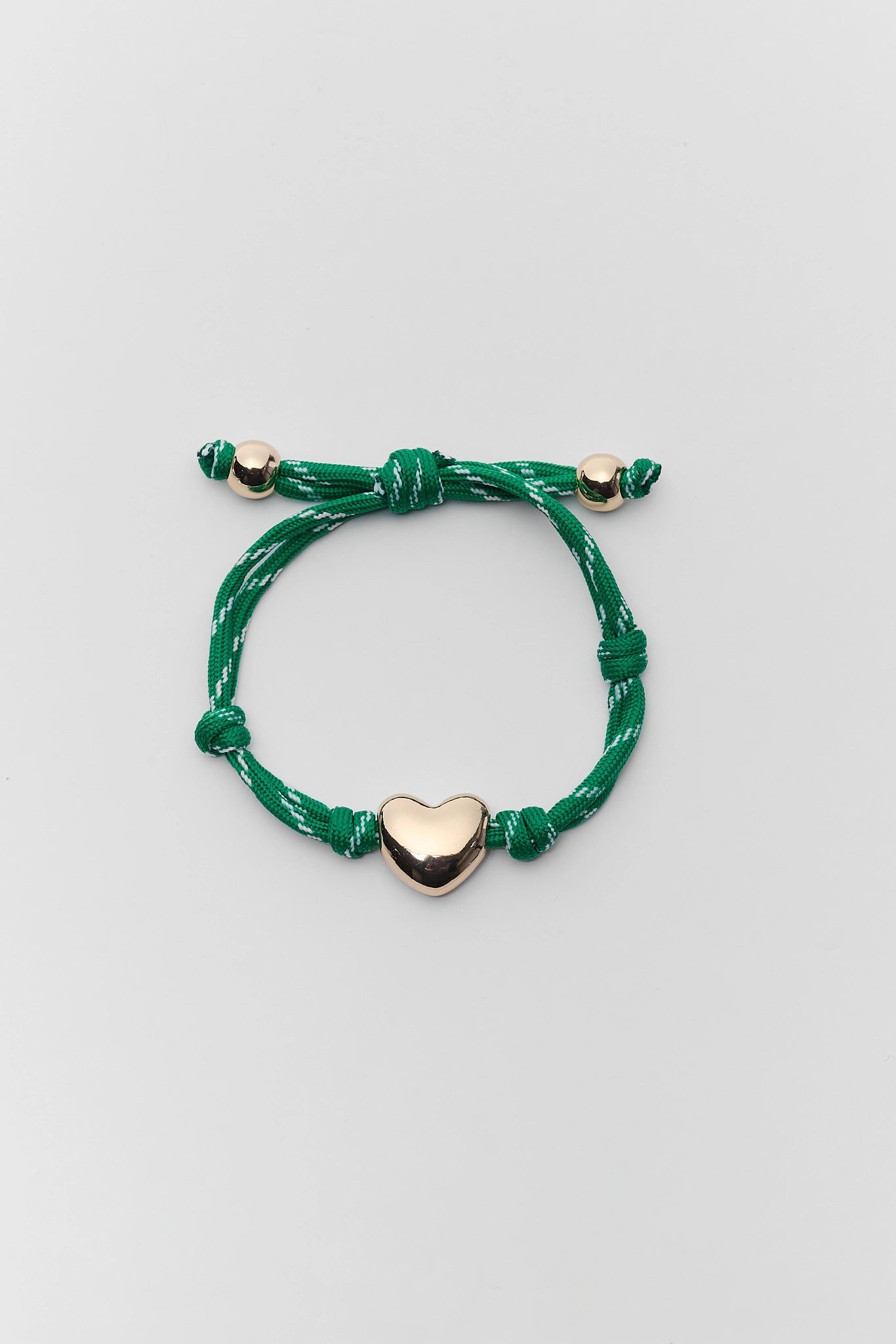Green bracelet with a gold heart charm on a light gray background