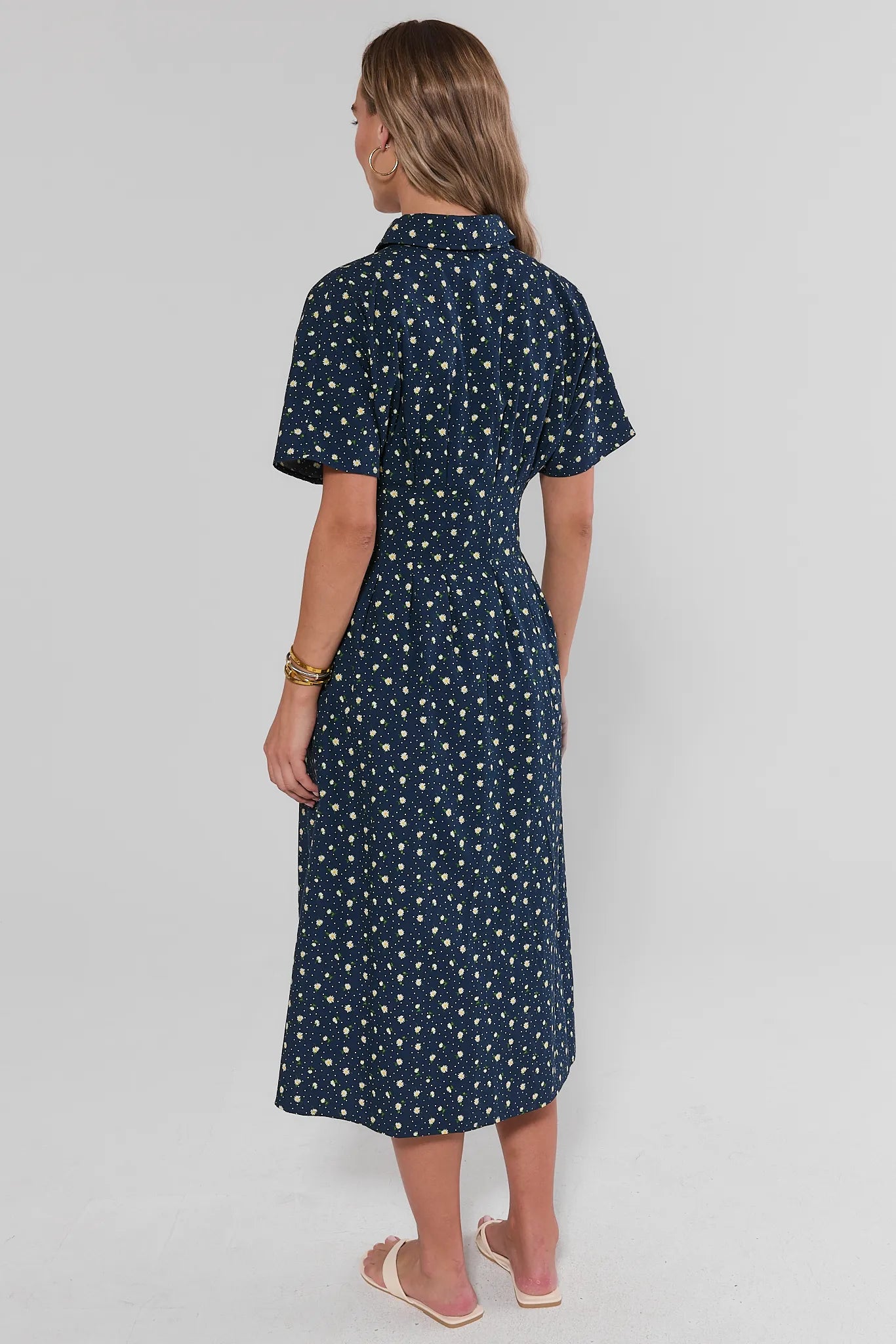 Woman standing wearing a navy dress with white patterns on a light gray background
