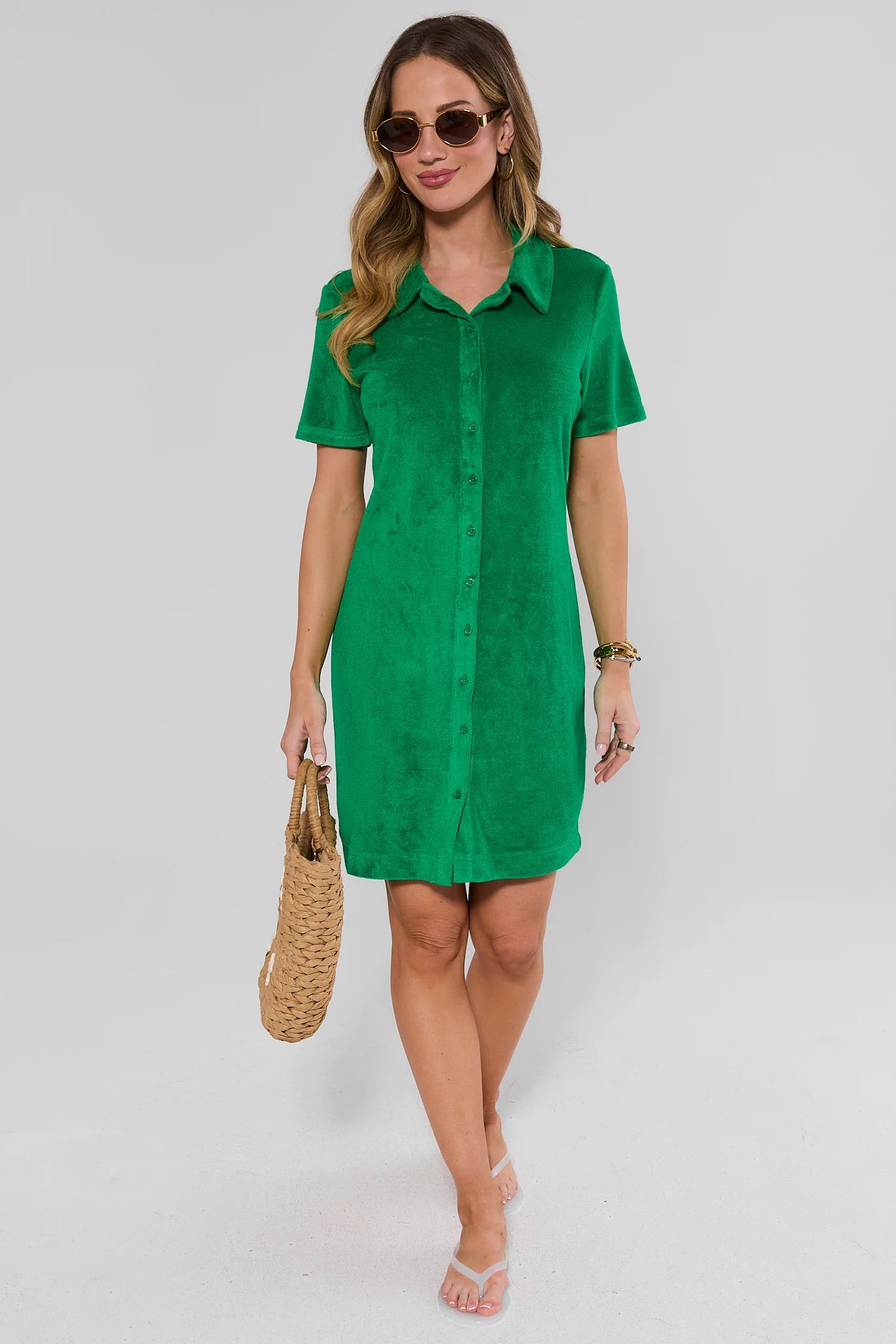 Woman wearing a green dress holding a woven bag on a plain background stand