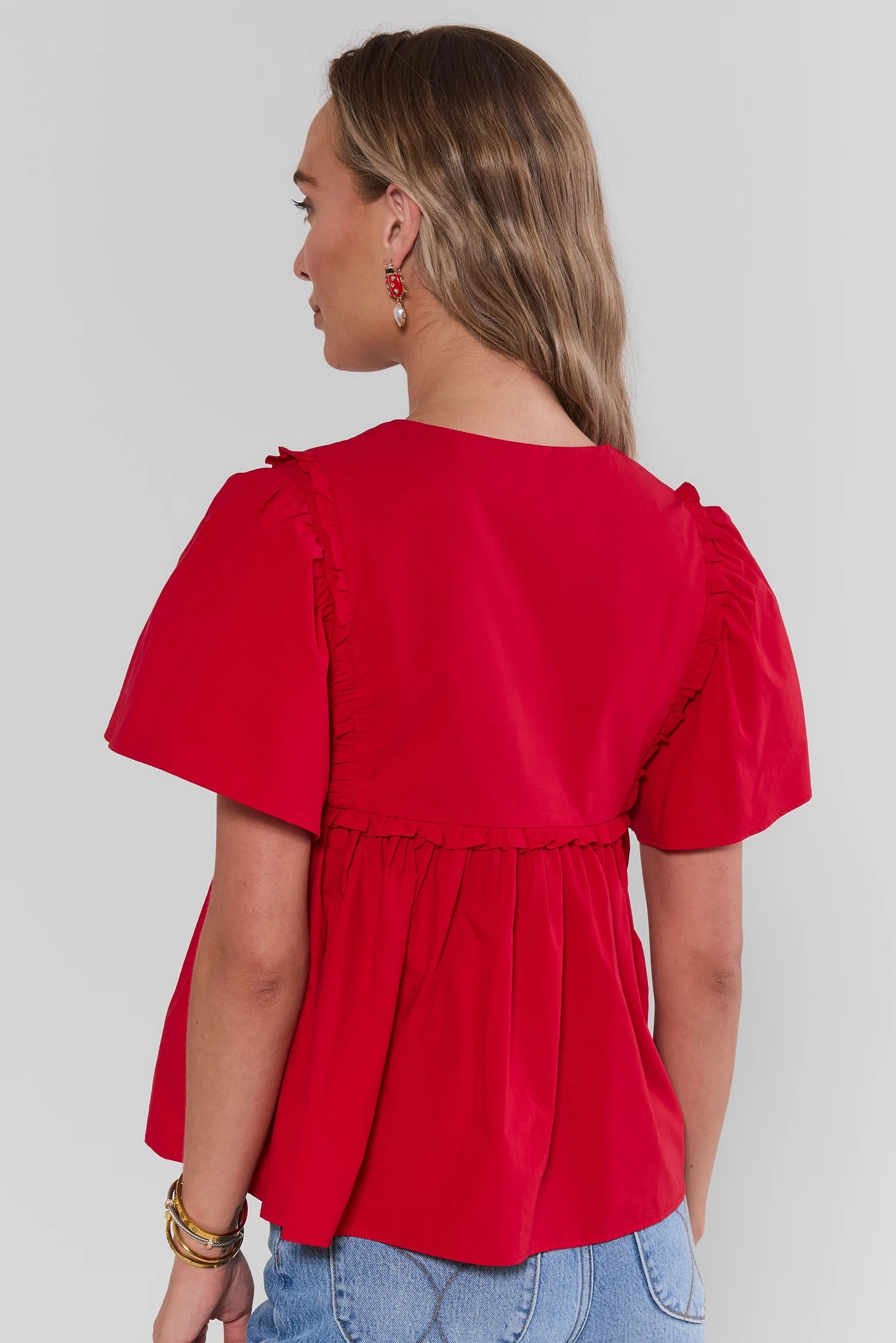 Woman wearing a red blouse with puff sleeves against a plain background stand
