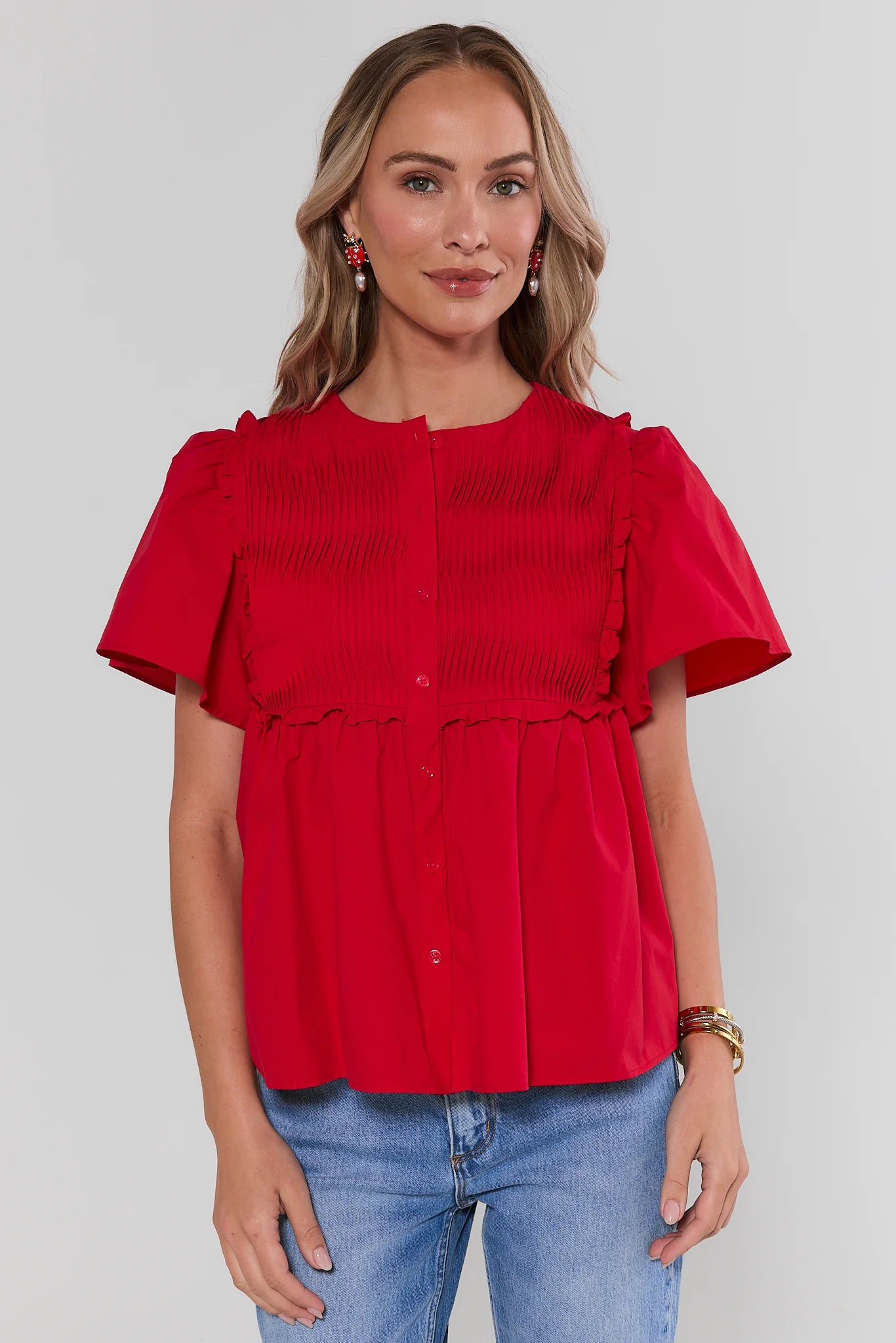 Woman wearing a red blouse with ruffled details and blue jeans on a plain background