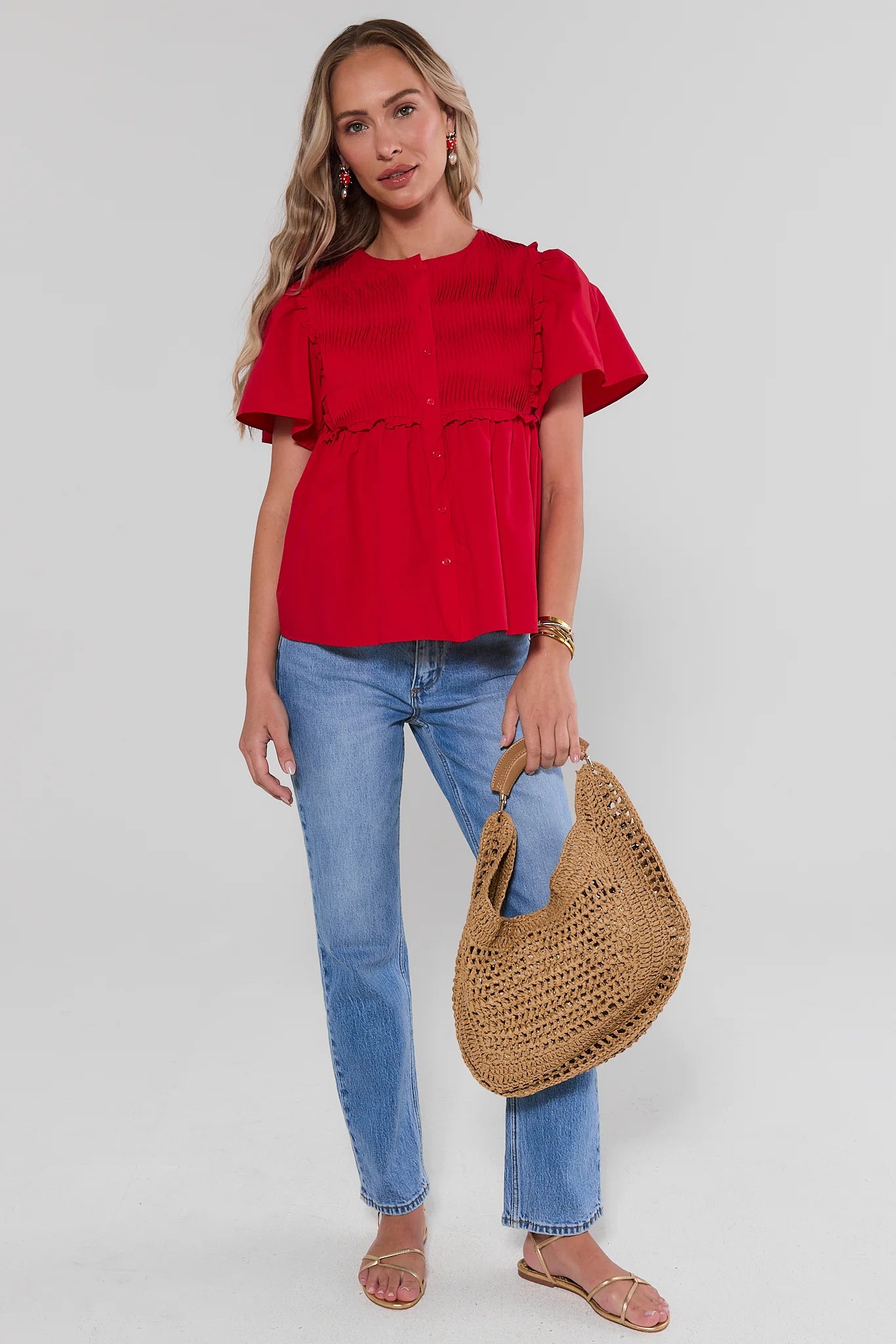 Woman wearing a red top and blue jeans, holding a straw bag on a white background