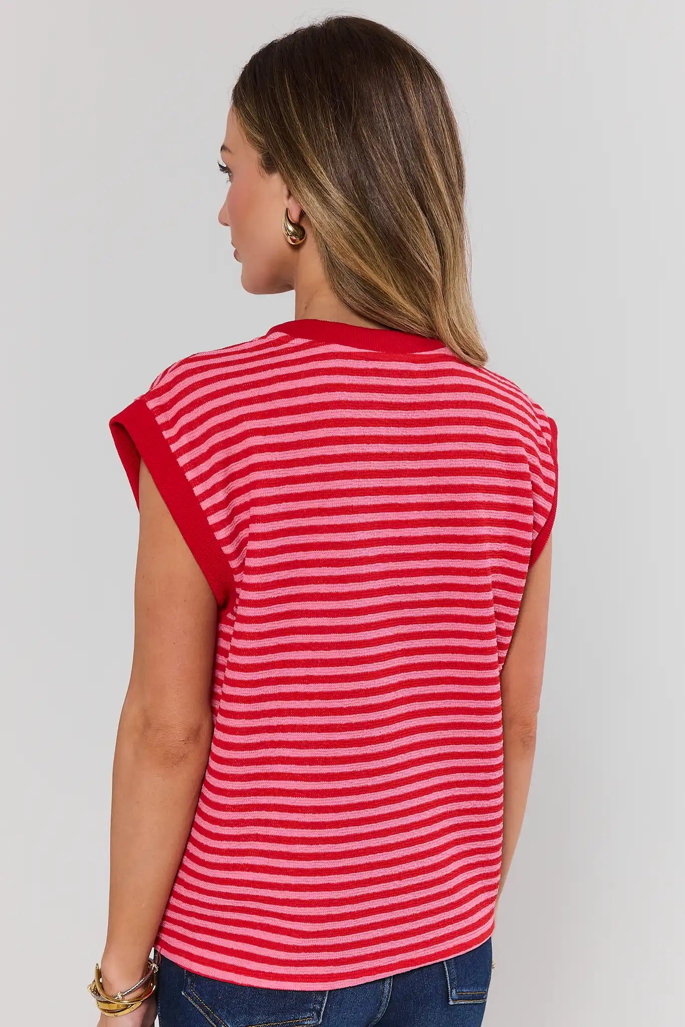 Woman standing wearing a red and white striped sleeveless top against a plain background