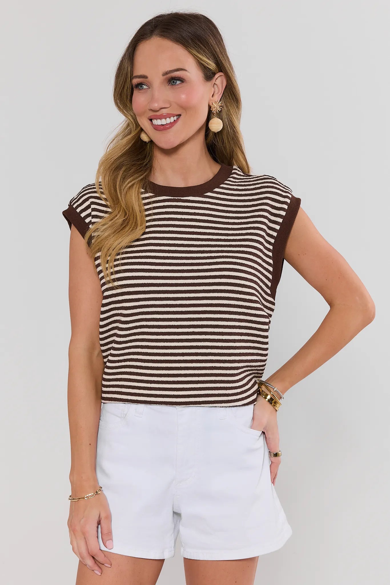 Woman wearing a brown and beige striped top with white shorts on a plain background