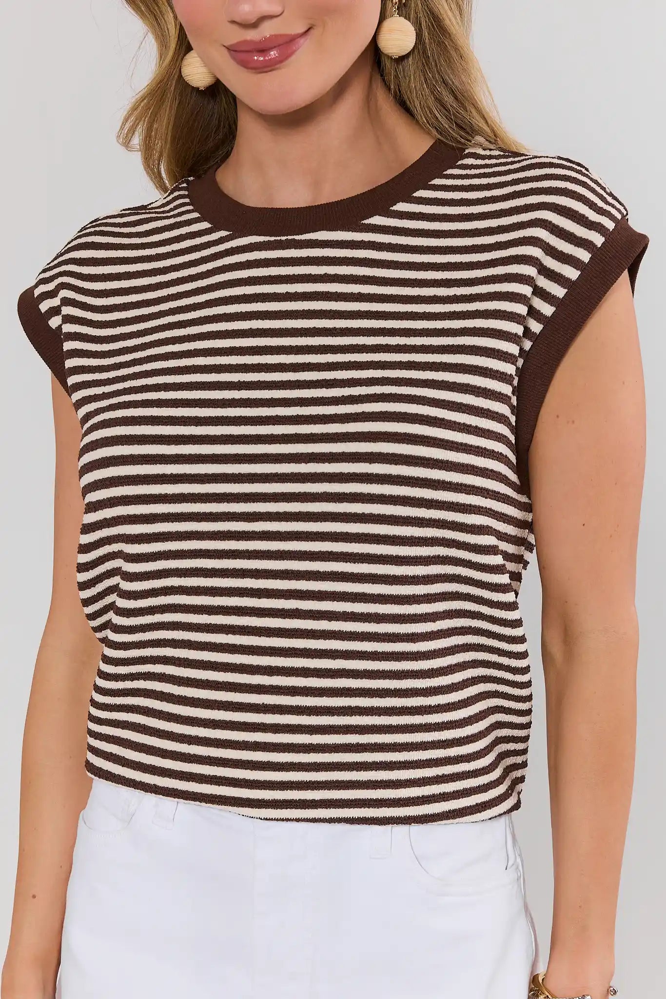 close up Woman wearing a brown and white striped sleeveless top against a plain background