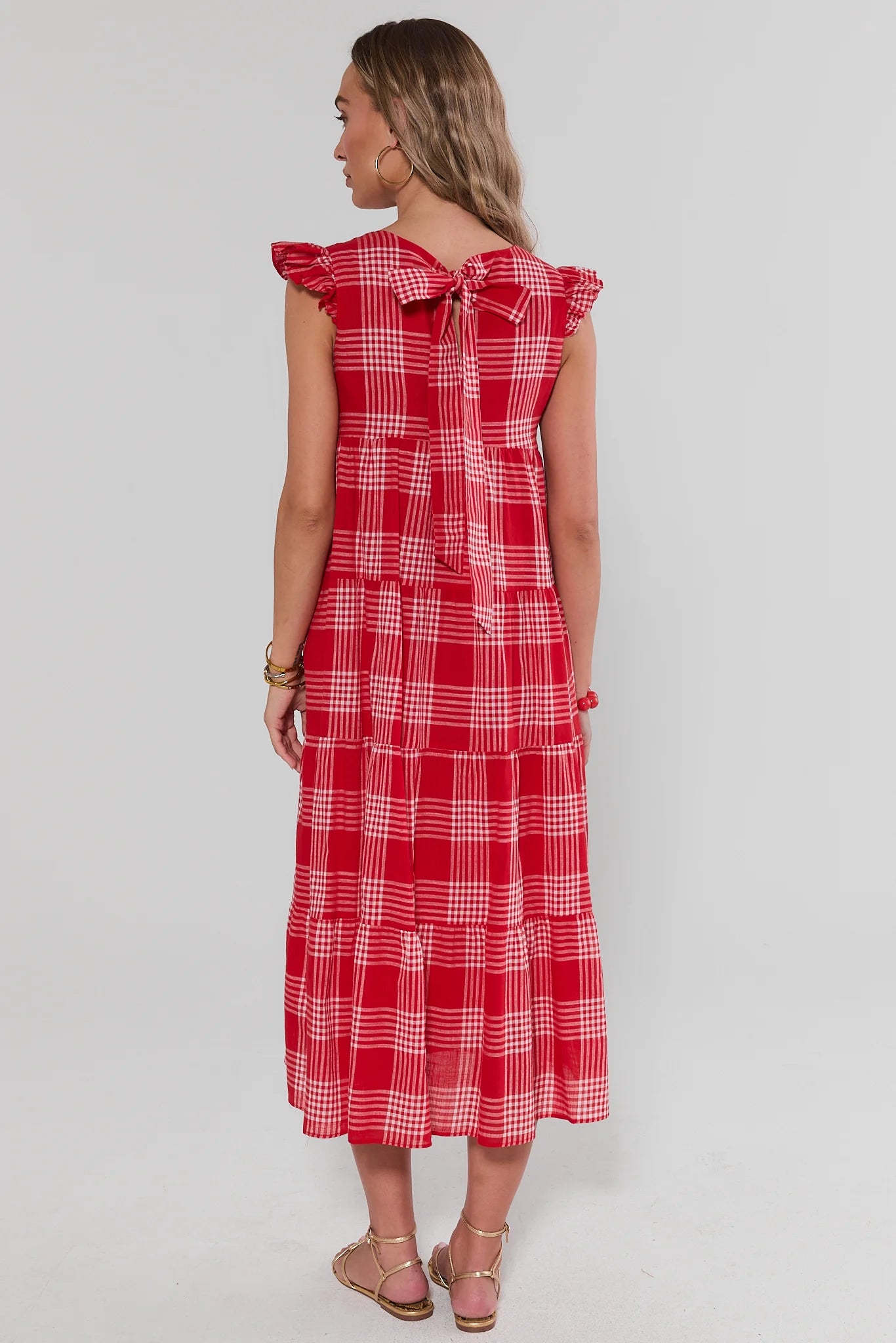 Woman standing wearing a red checkered dress on a plain background