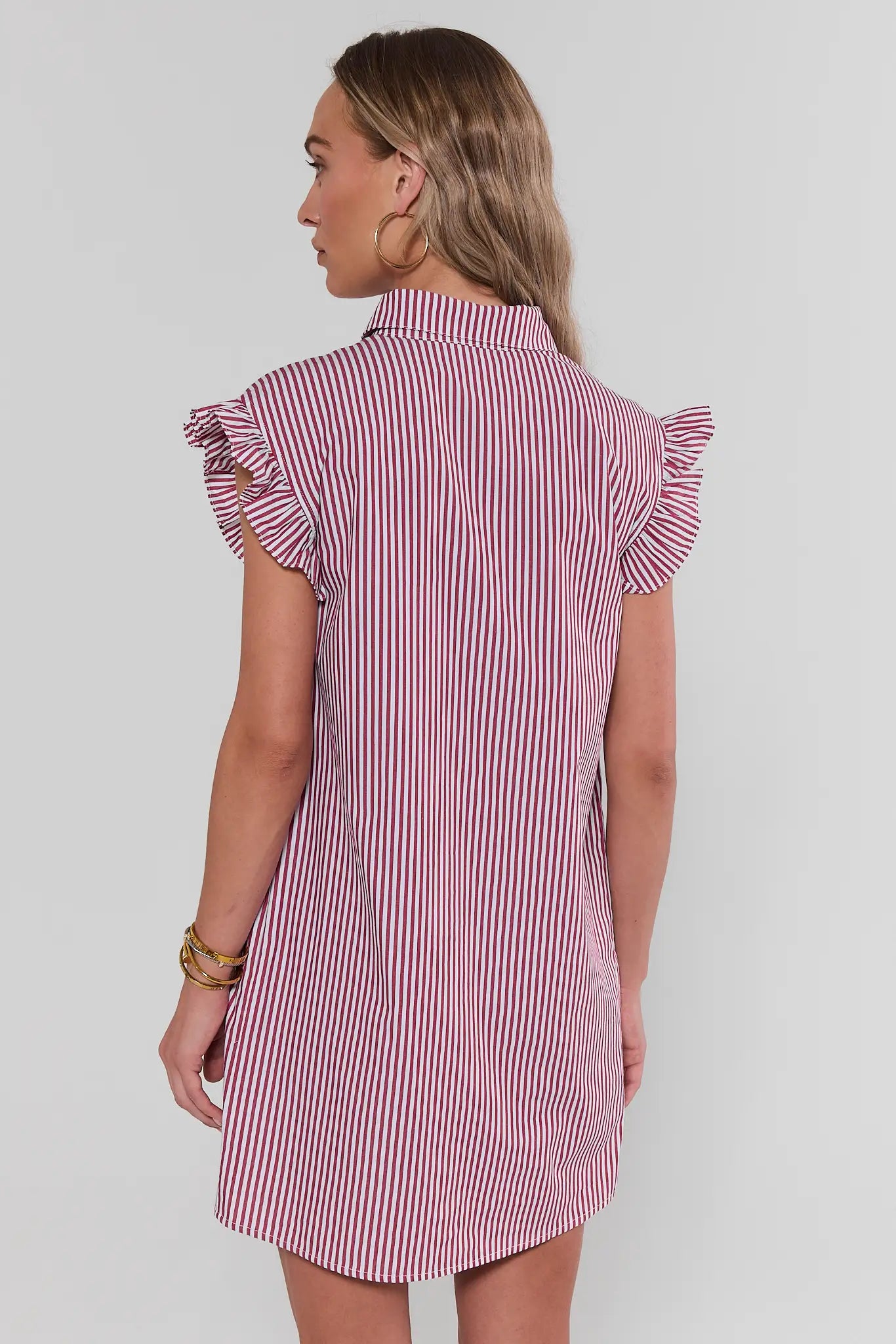 Woman wearing a red and white striped dress with ruffled sleeves on a plain background standing