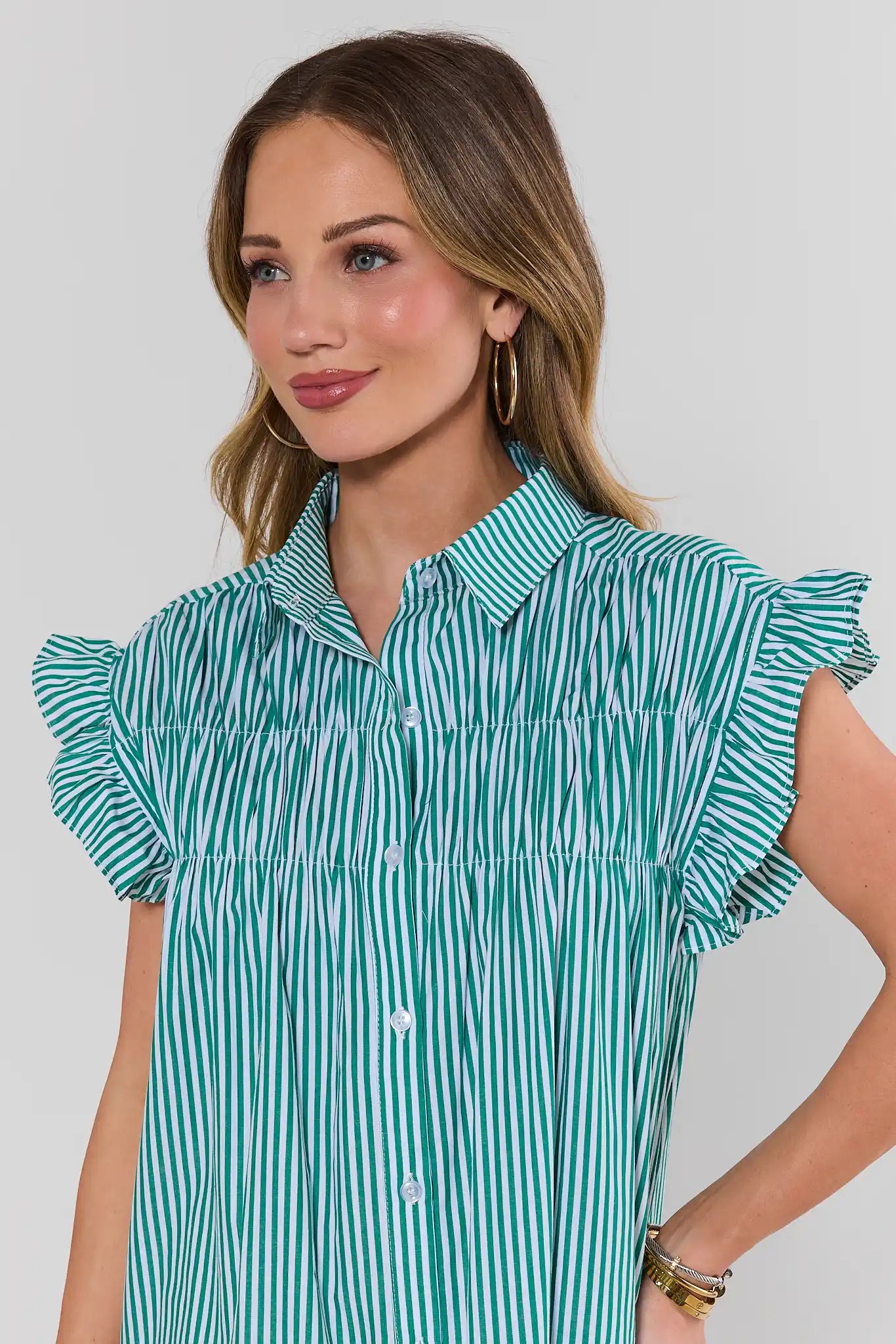 Woman wearing a green and white striped shirt with ruffled sleeves on a plain background close up