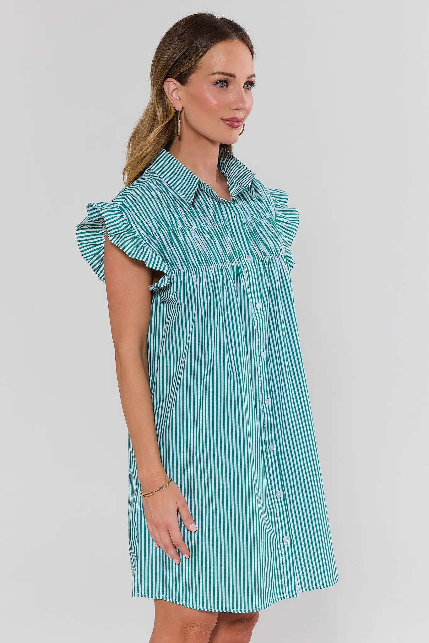 Woman side shot wearing a green and white striped dress against a plain background