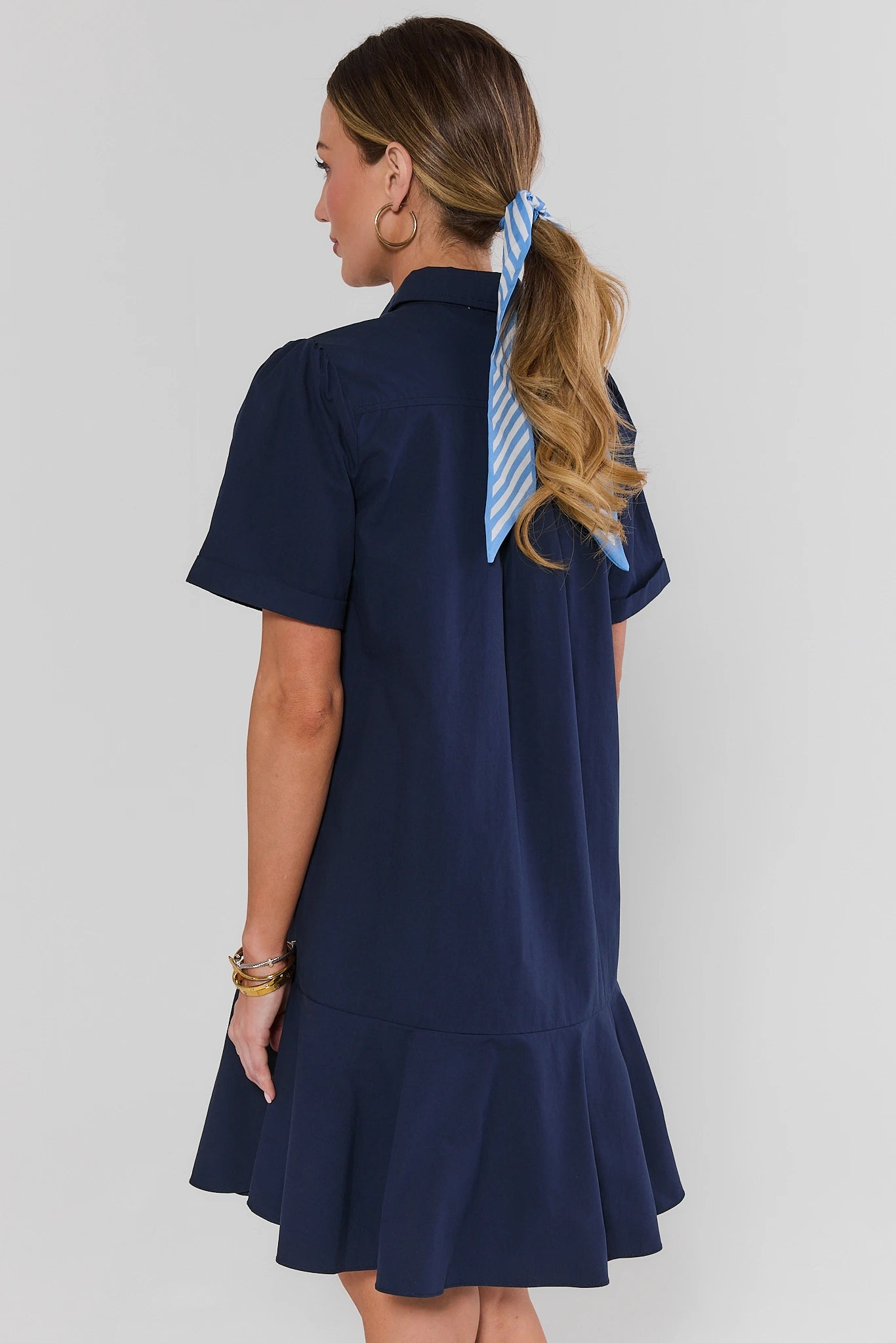 Woman standing wearing a navy dress with a blue ribbon in her hair on a white background