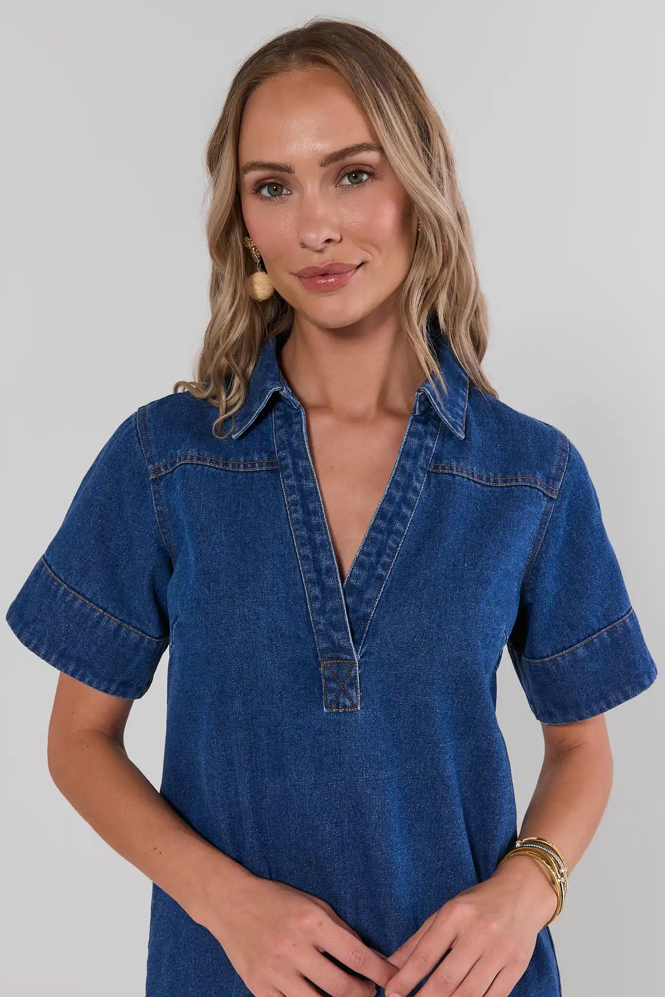 Woman wearing a blue denim dress against a plain background close up