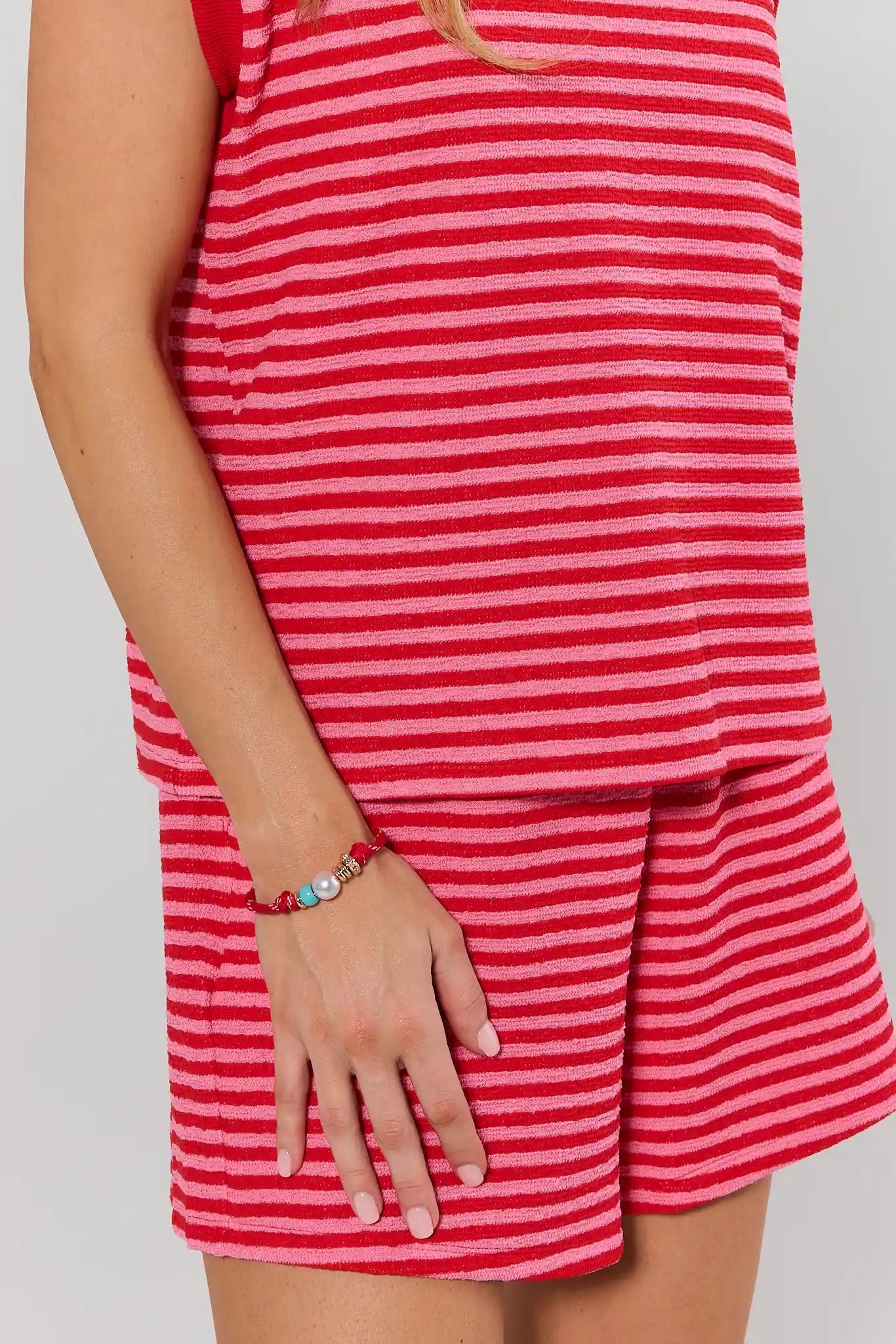 Person wearing a red and white striped set with bracelet on a plain background