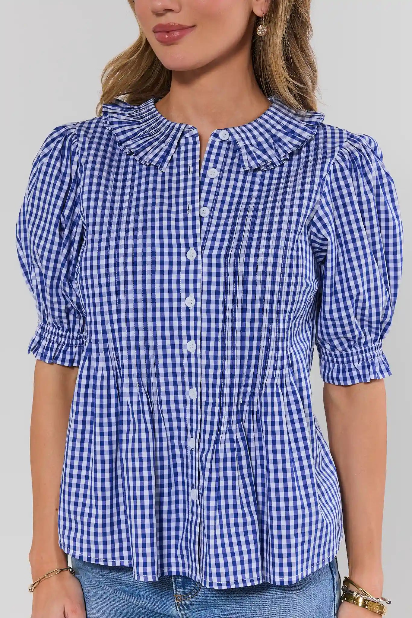 Woman wearing a blue and white checkered blouse with puffed sleeves on a plain background close up