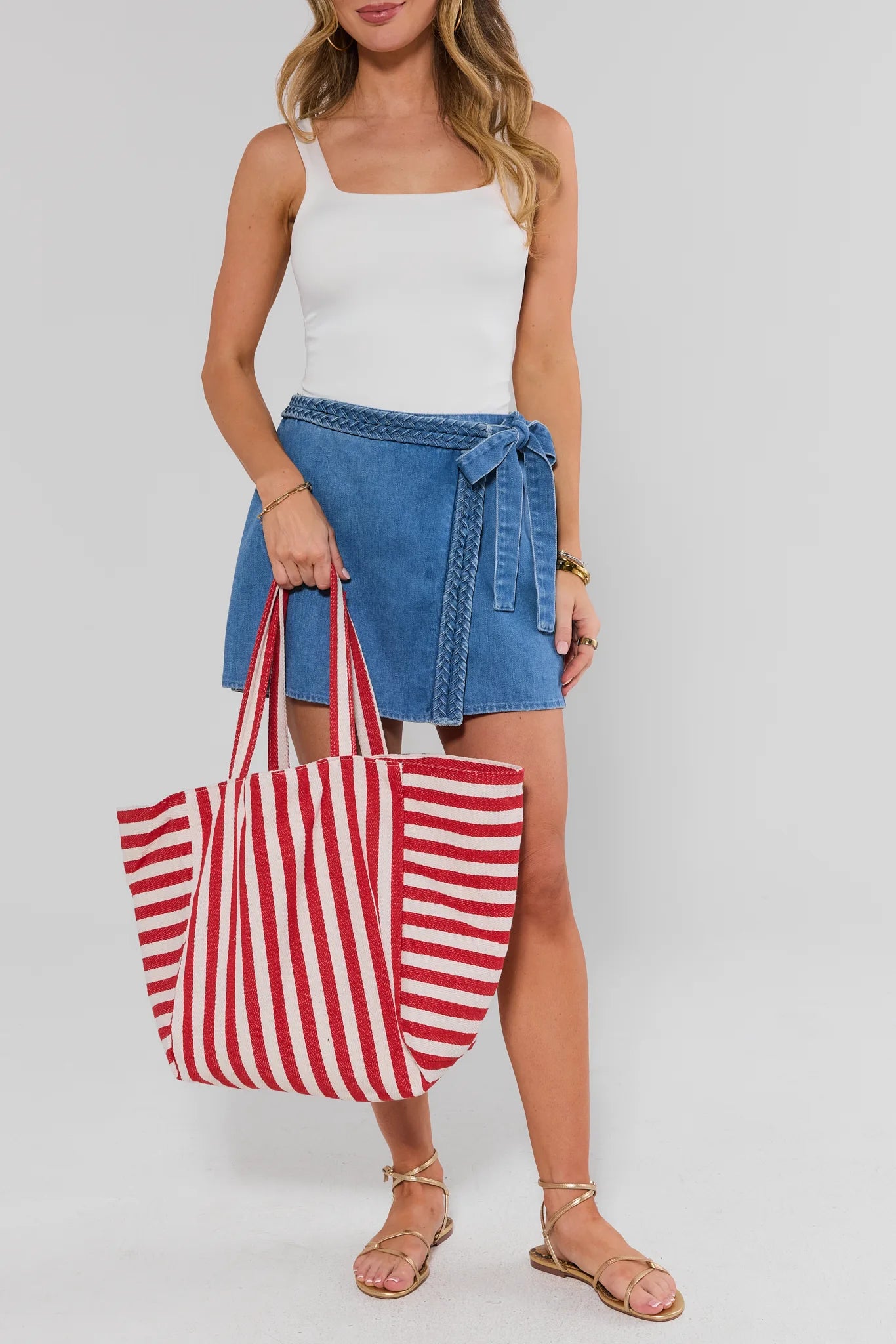 Woman holding a red and white striped tote bag against a plain background
