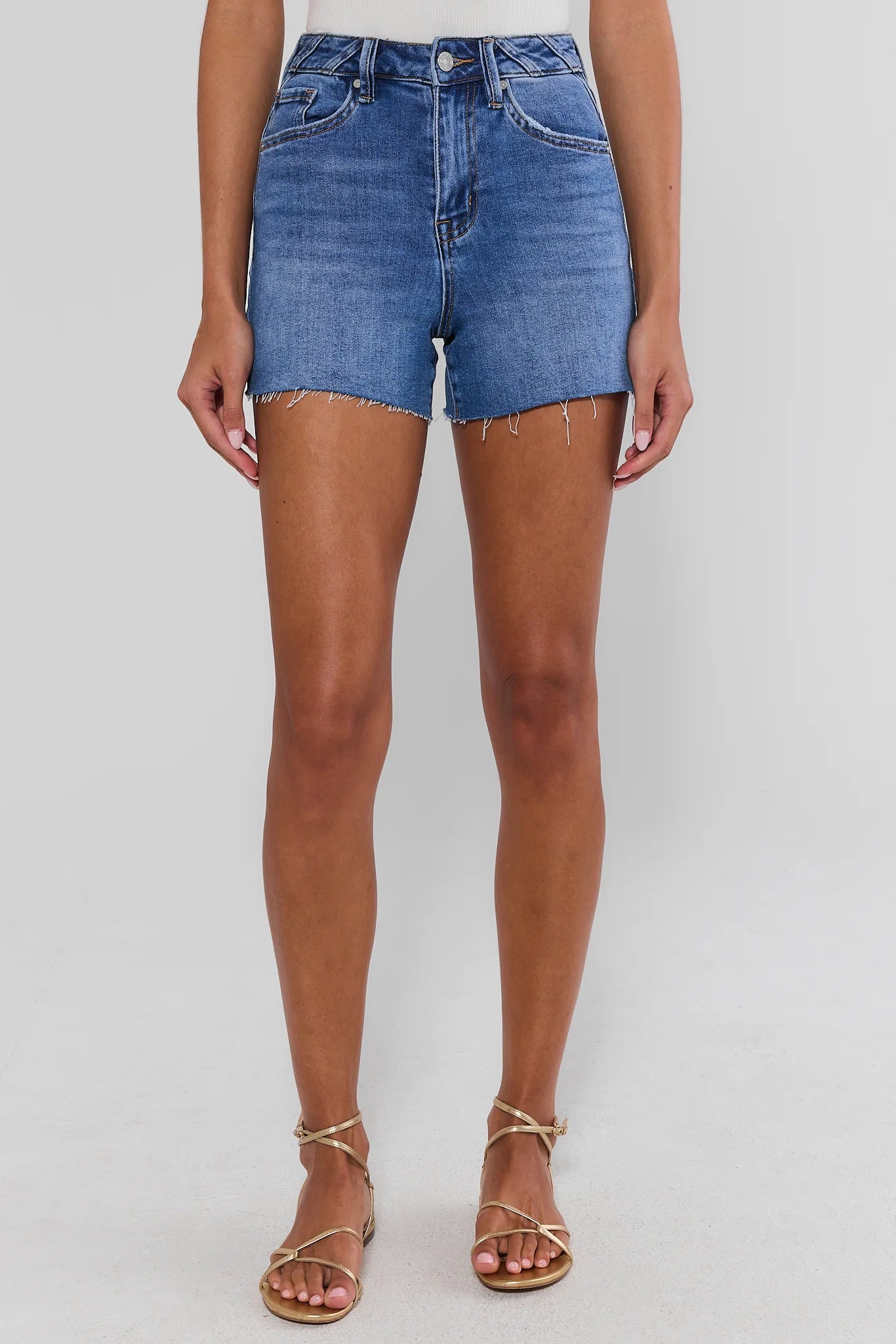 woman standing wearing medium wash shorts on white background