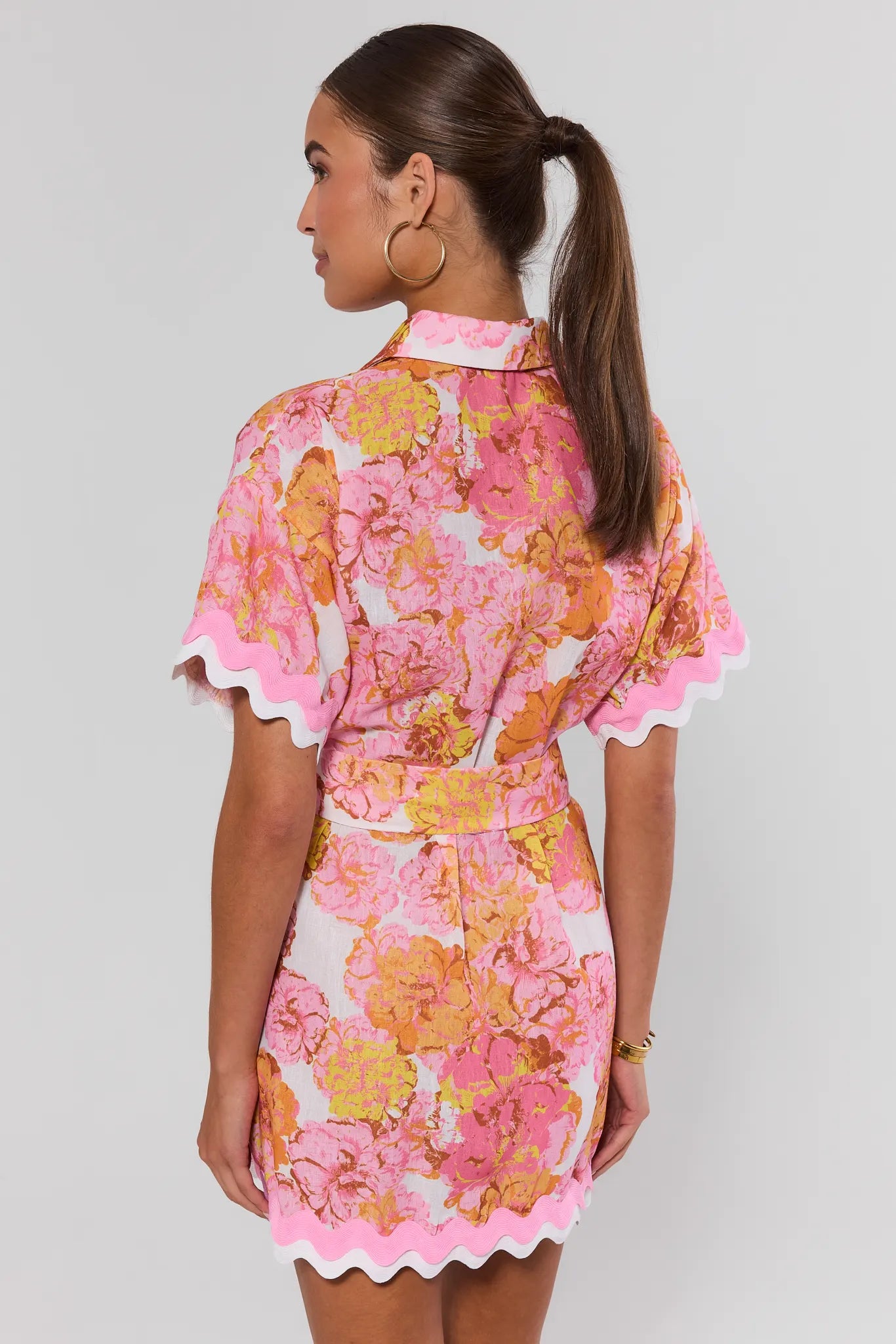 Woman wearing a pink floral dress on a plain background stand