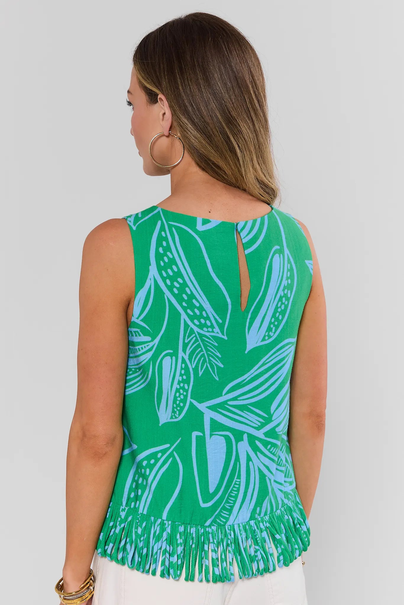 Woman wearing a green sleeveless top with white leaf pattern on a plain background walking