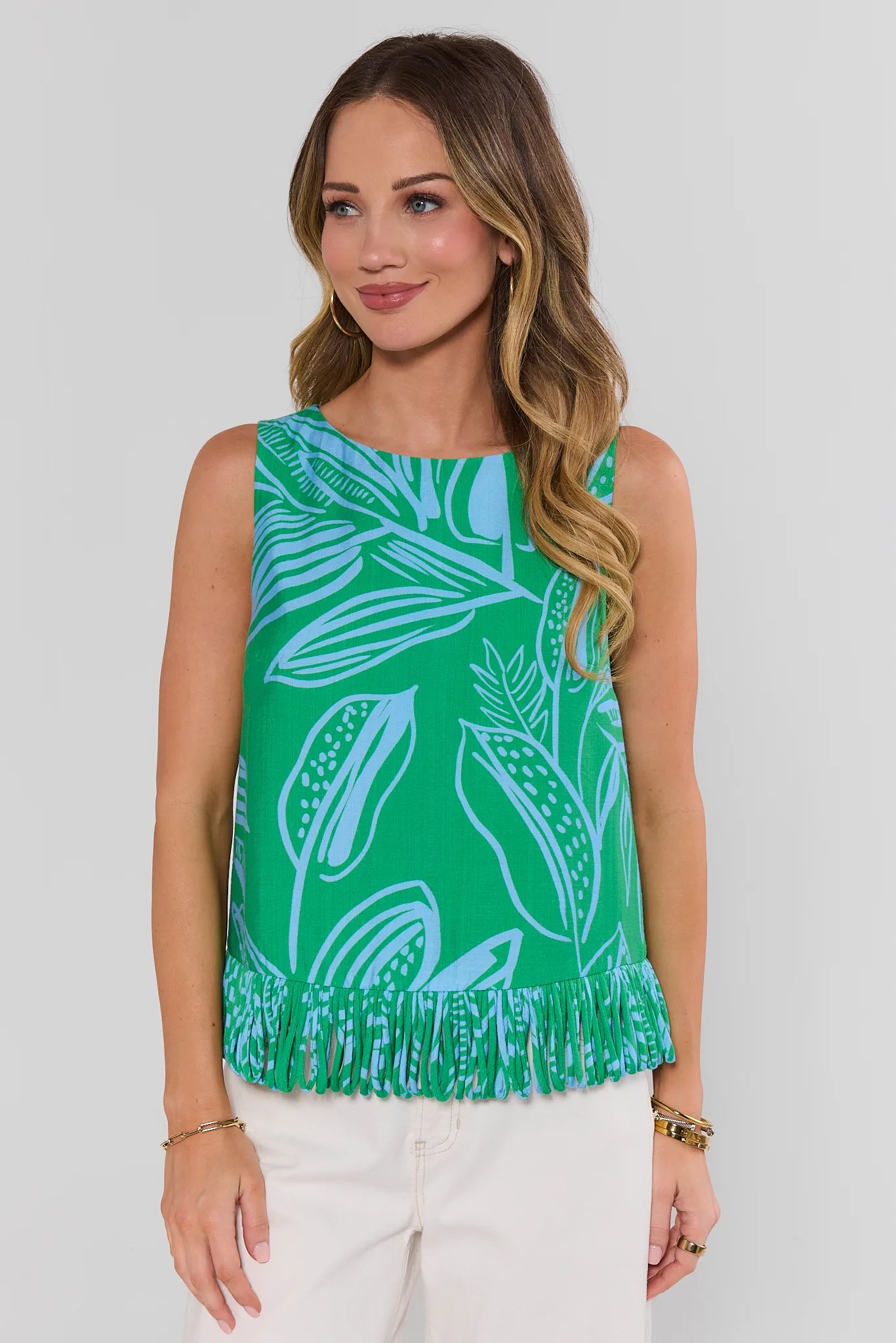 Woman wearing a green sleeveless top with white leaf pattern and fringes on a plain background