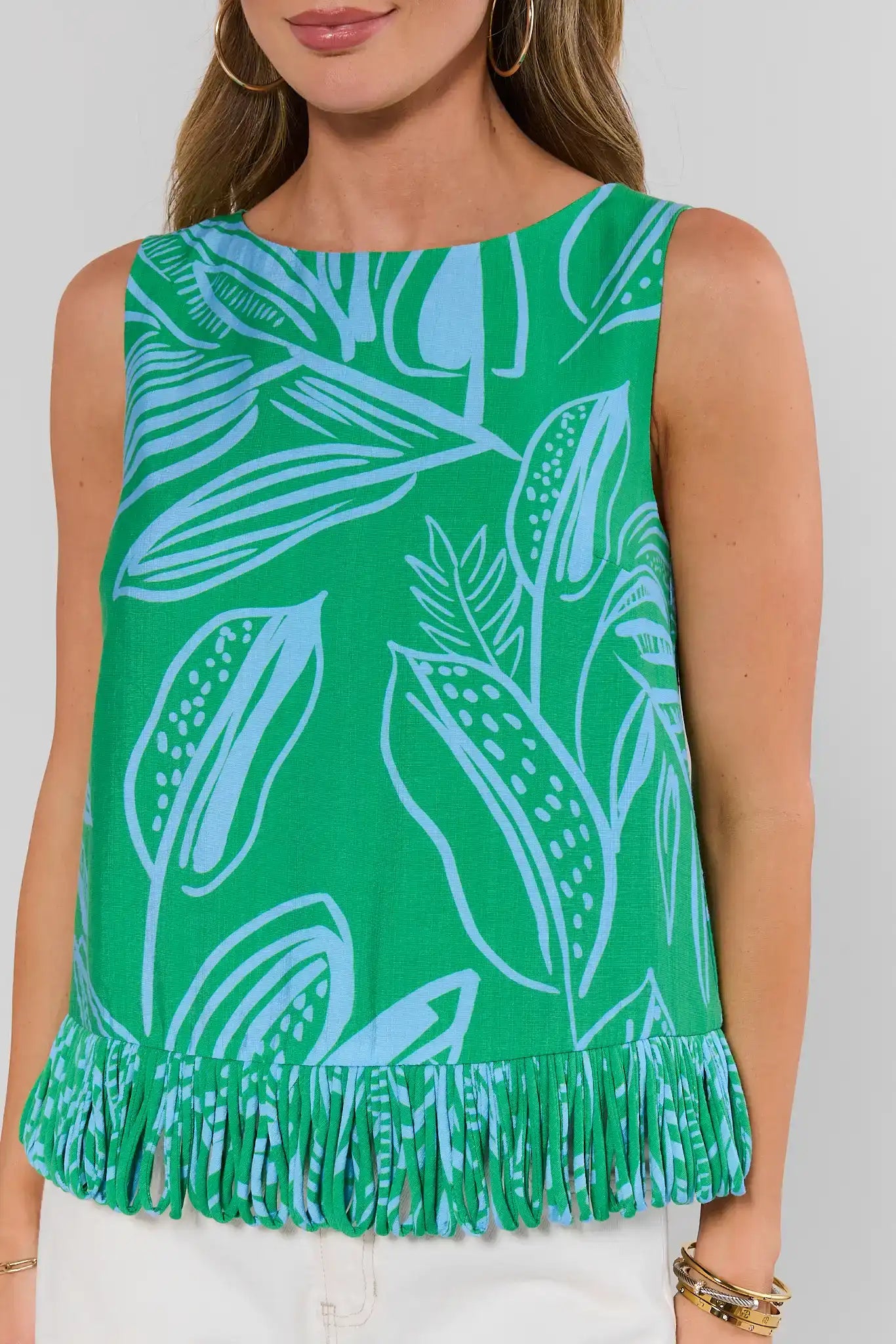 Woman wearing a green sleeveless top with white leaf pattern and frayed hem on a plain background close up