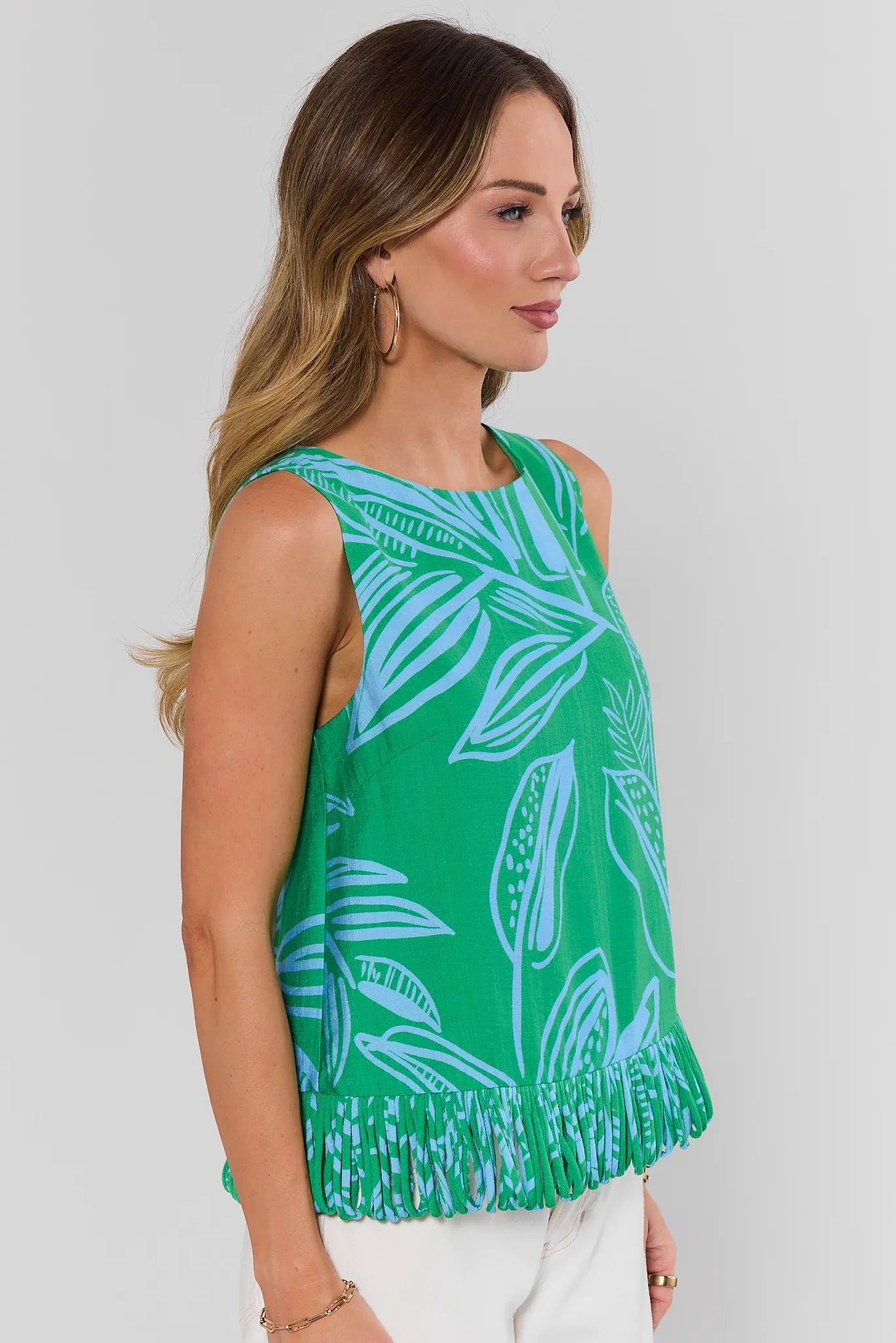 Woman wearing a green sleeveless top with white leaf pattern on a plain background side