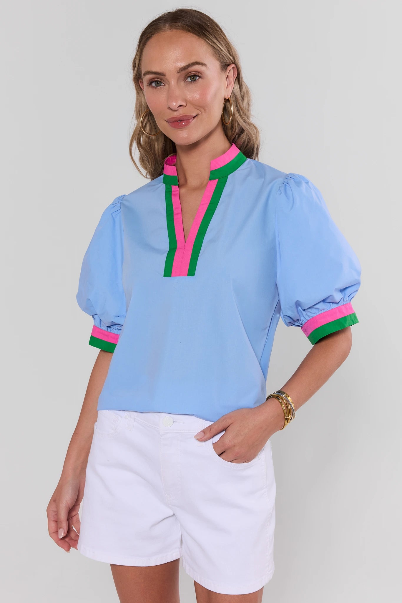 Woman wearing a light blue blouse with colorful accents and white shorts on a plain background