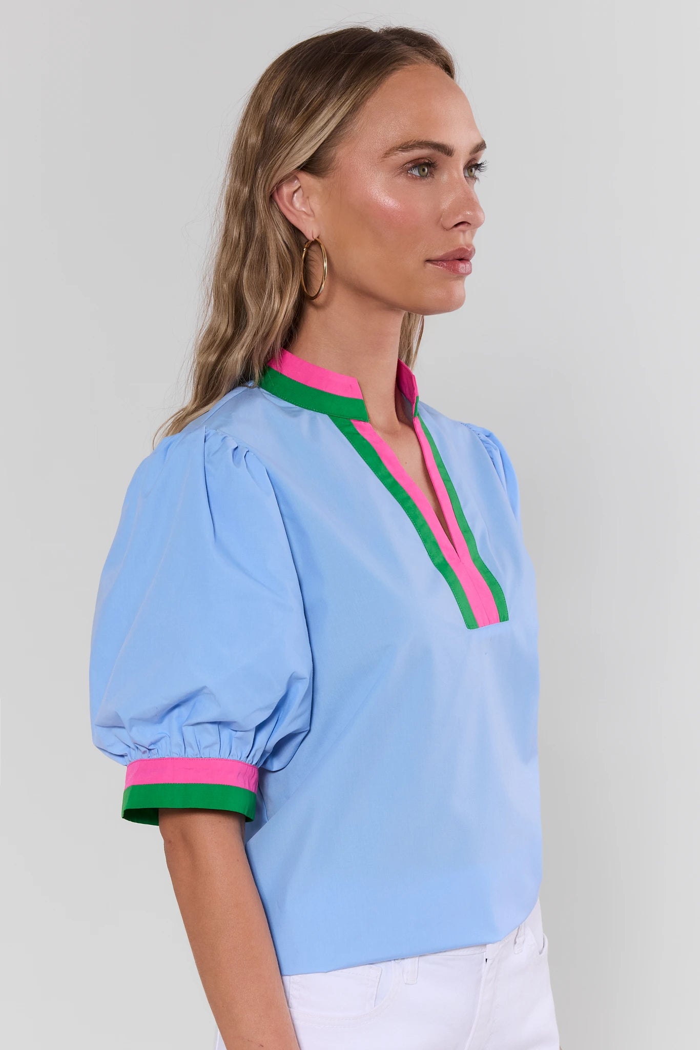 Woman wearing a light blue blouse with colorful trim on a plain background side