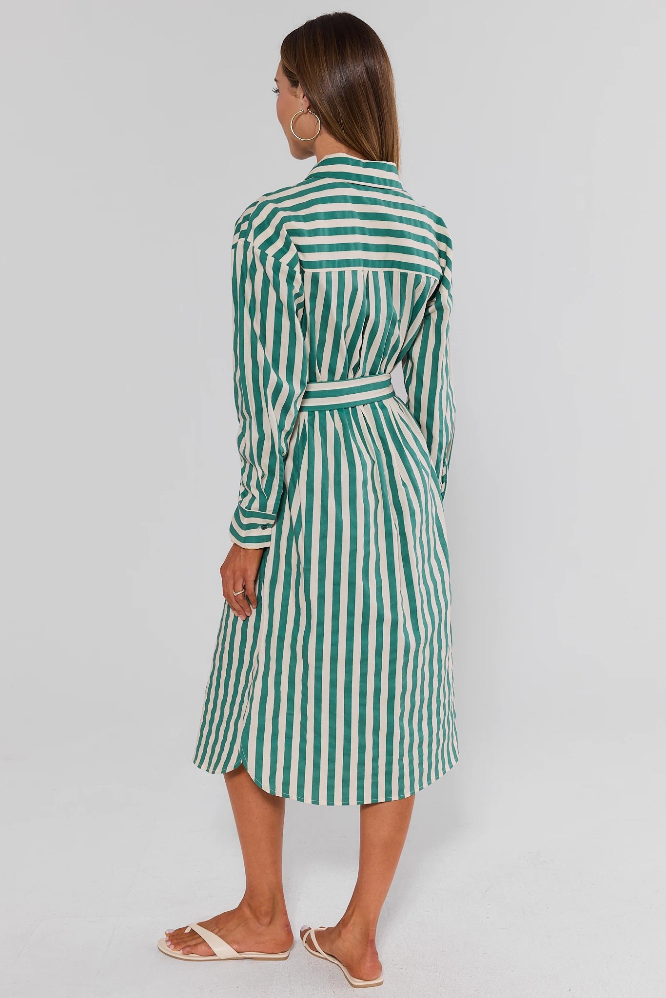 Woman standing wearing a green and white striped dress on a plain background