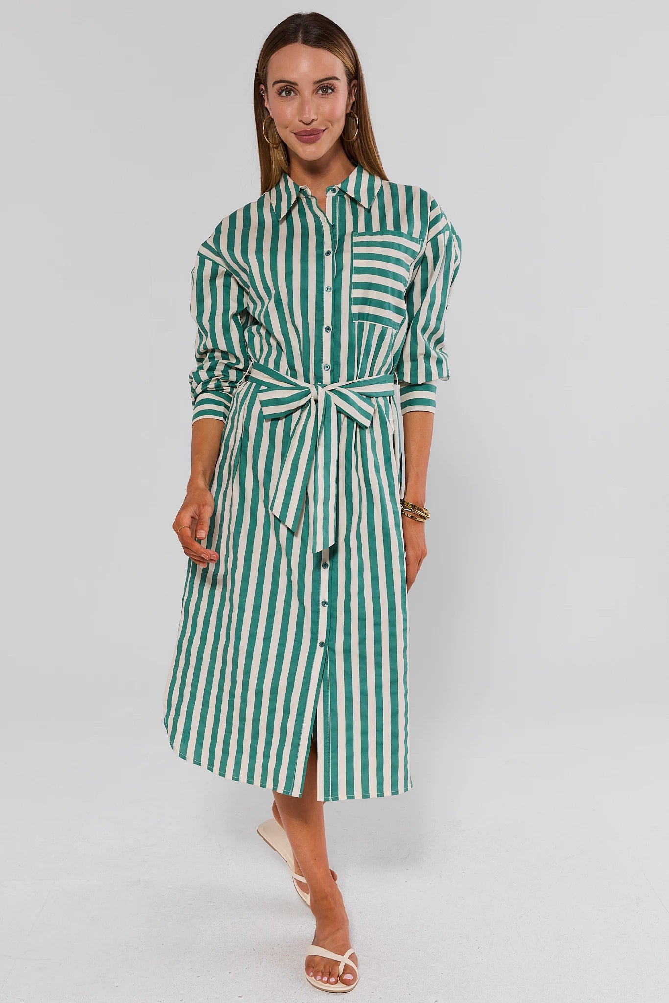 Woman wearing a green and white striped dress on a gray background walking