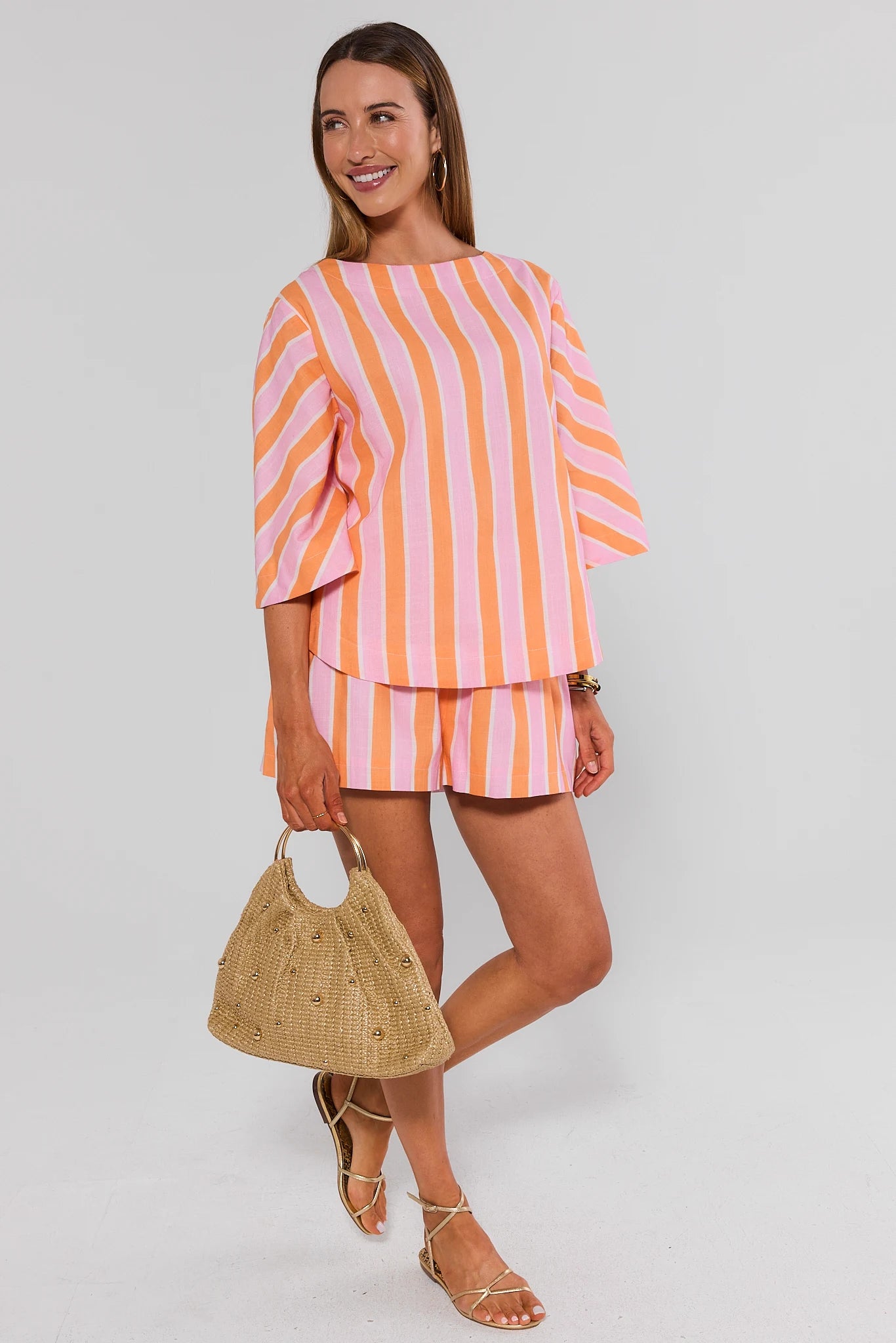 Woman wearing a pink and orange striped outfit with a beige handbag on a white background