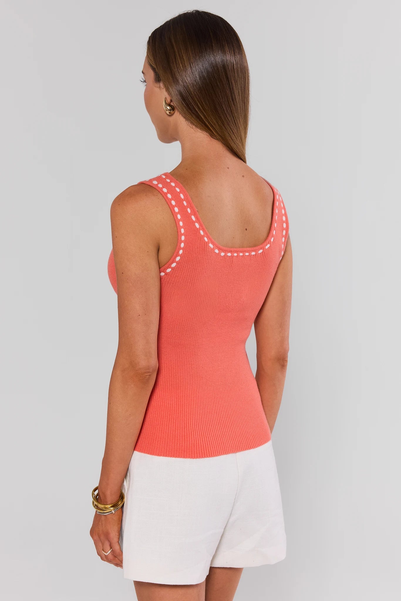 Woman wearing a coral tank top with white trim on a plain background standing