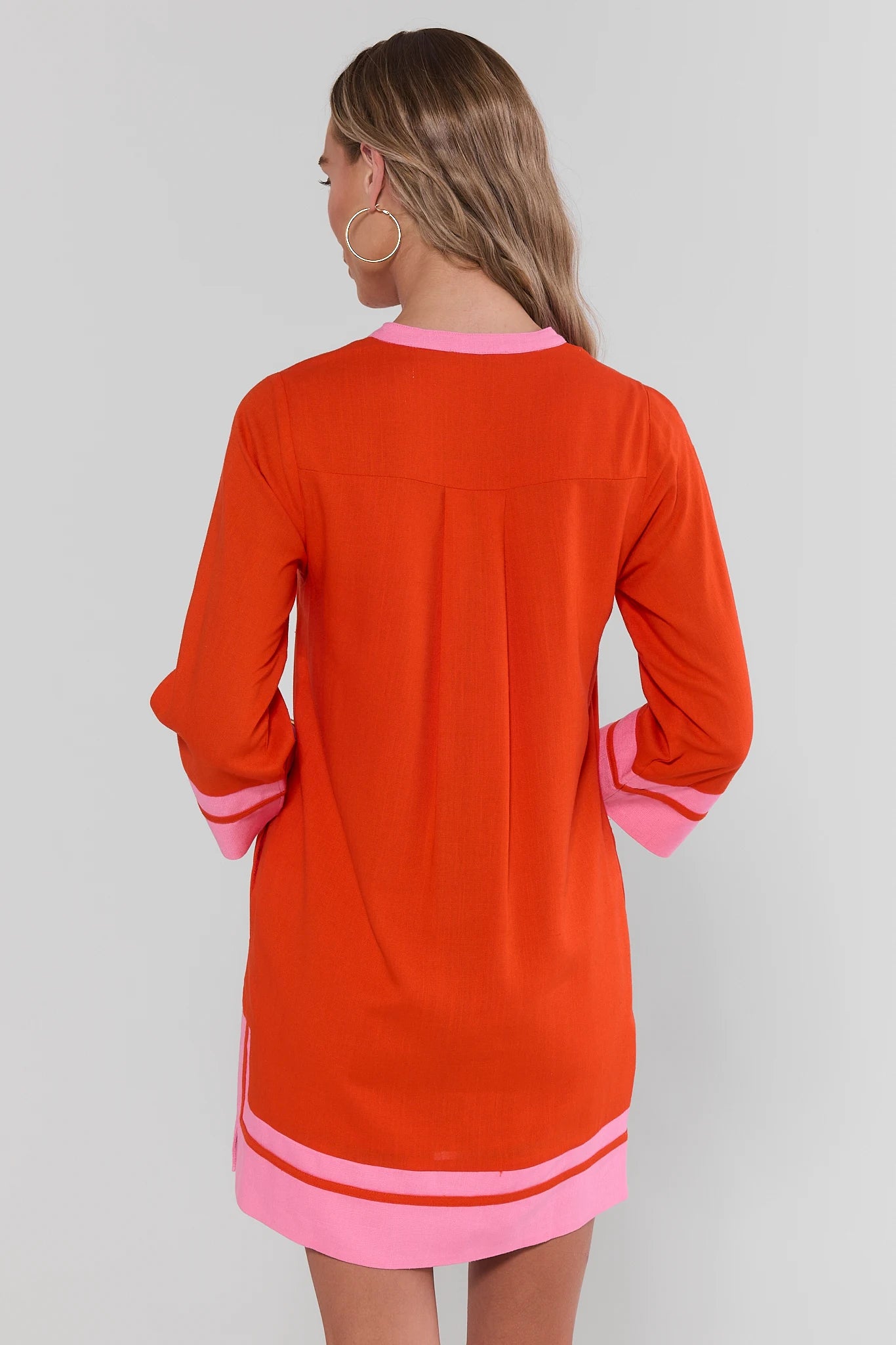 Woman standing wearing an orange and pink dress with a plain background