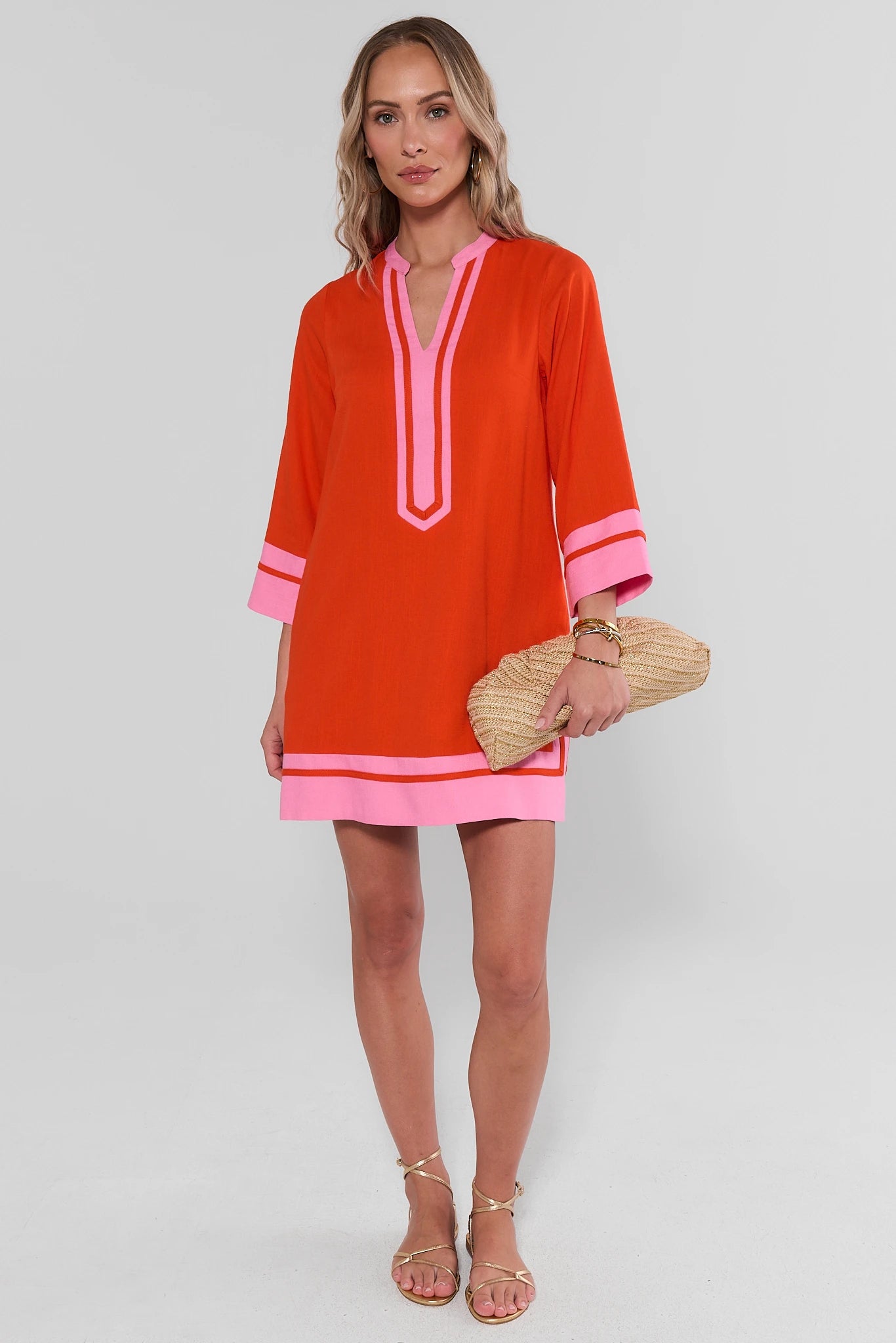 Woman wearing an orange and pink dress holding a clutch against a white background