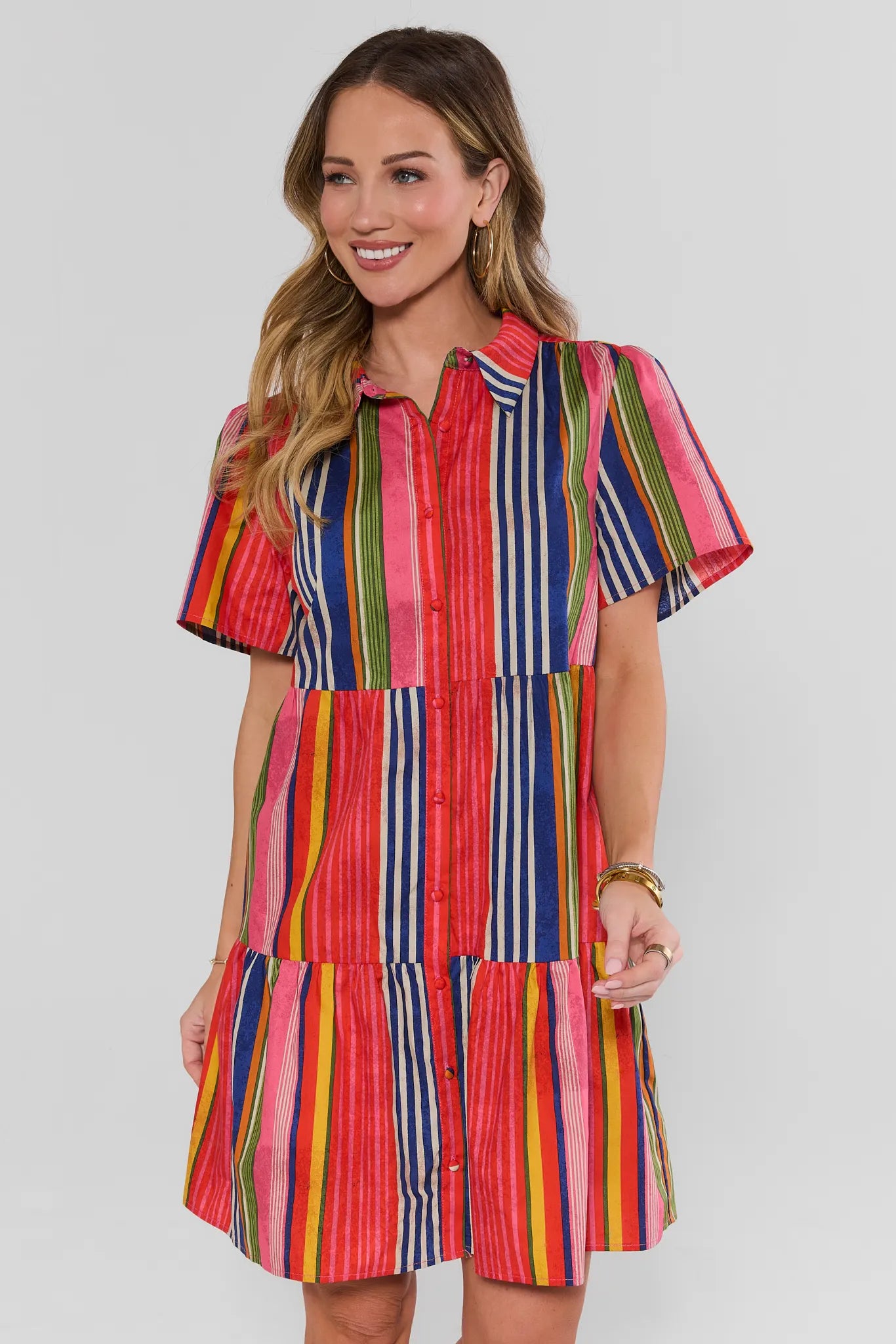 Woman wearing a colorful striped dress on a plain background standing