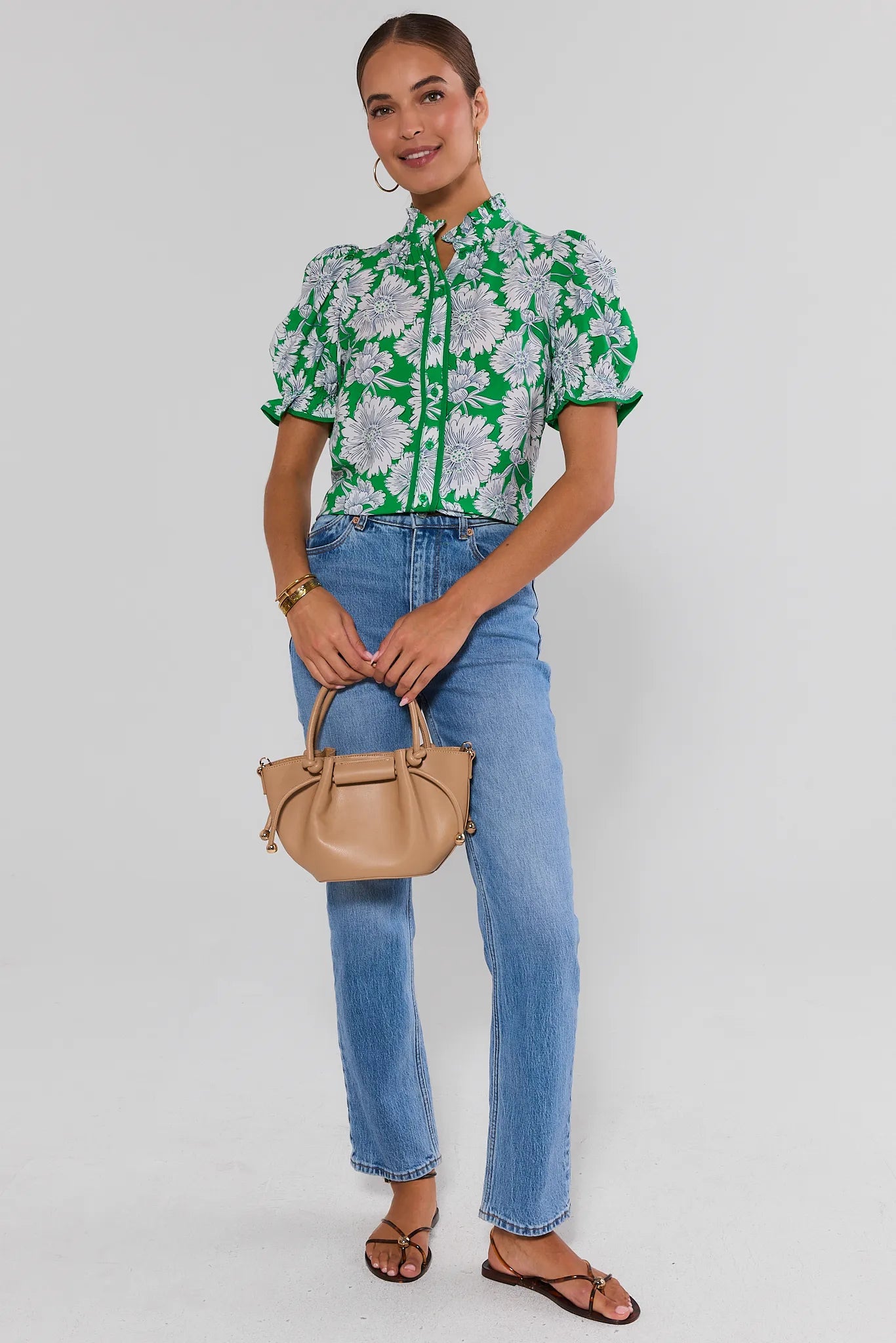 Woman wearing a green floral blouse, blue jeans, and holding a beige handbag on a white background