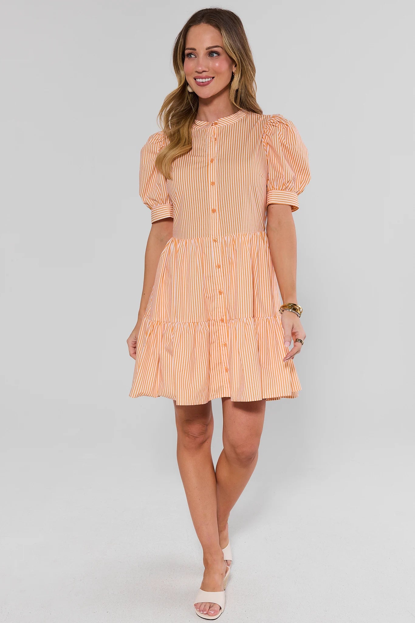 Woman wearing a peach-colored dress with puffed sleeves on a white background standing