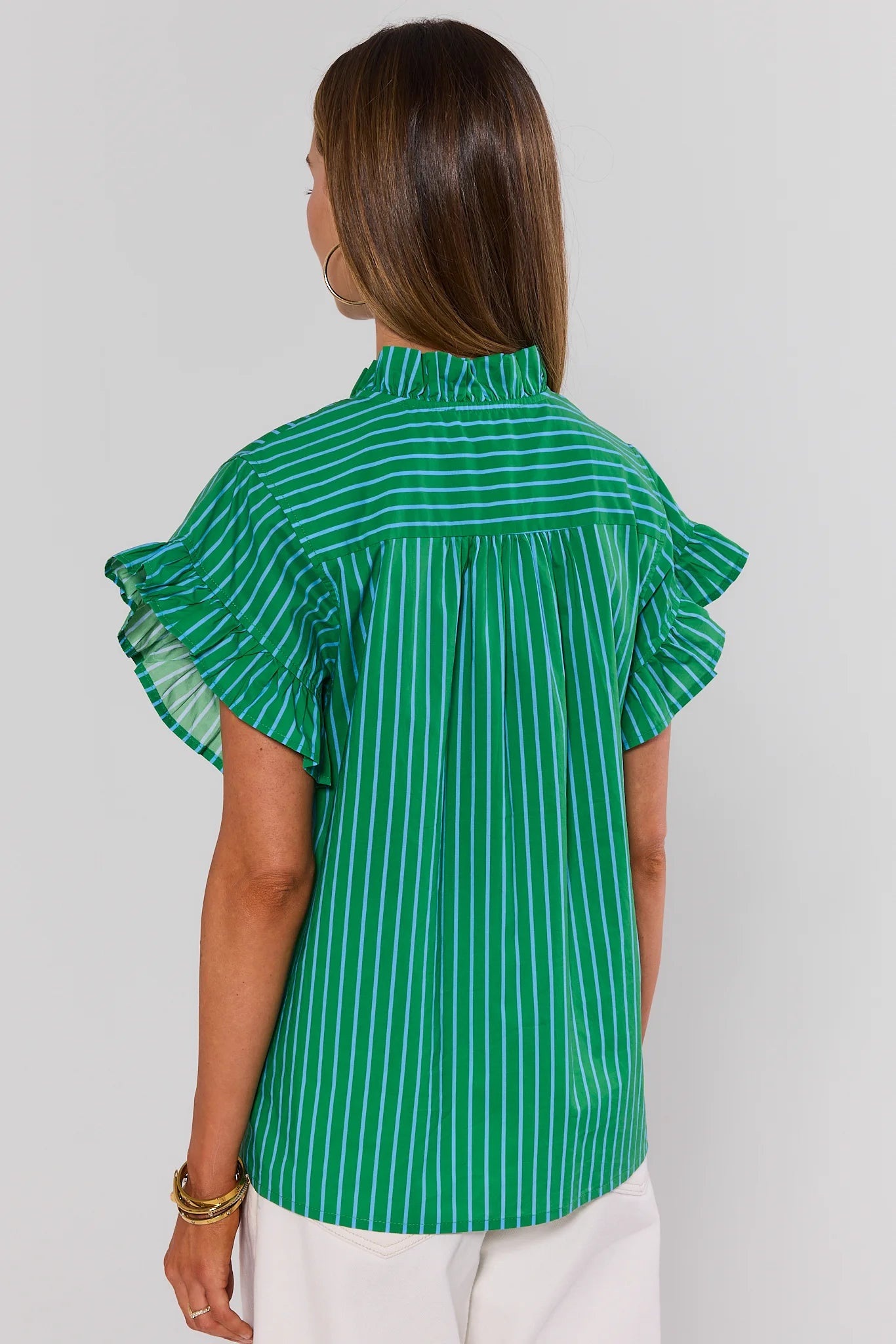 Woman wearing a green and white striped blouse with ruffled sleeves on a plain background standing