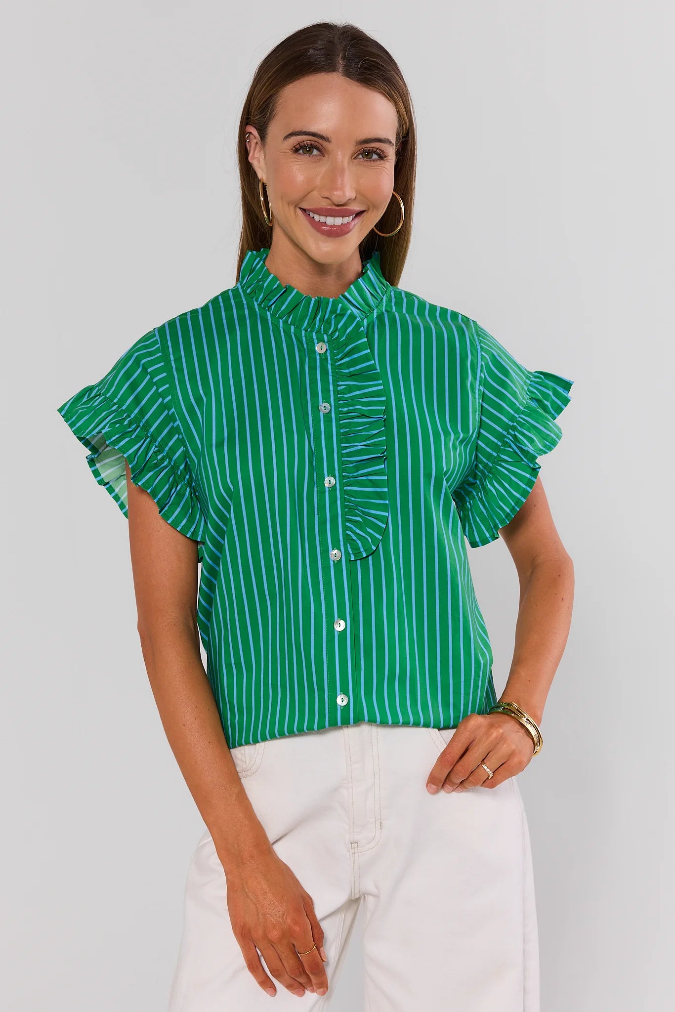 Woman wearing a green and white striped blouse with ruffled sleeves on a plain background