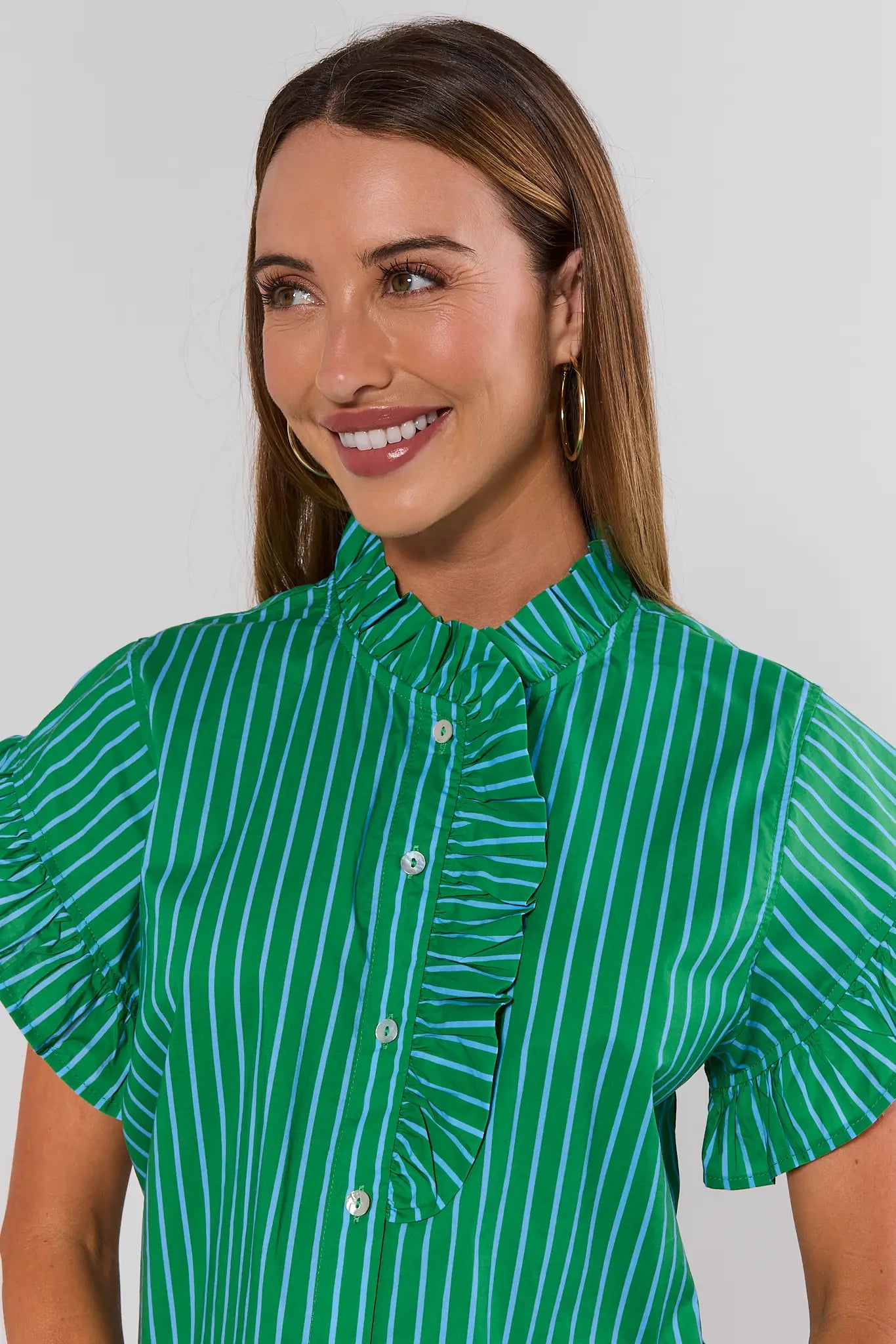Woman wearing a green and white striped blouse against a plain background close