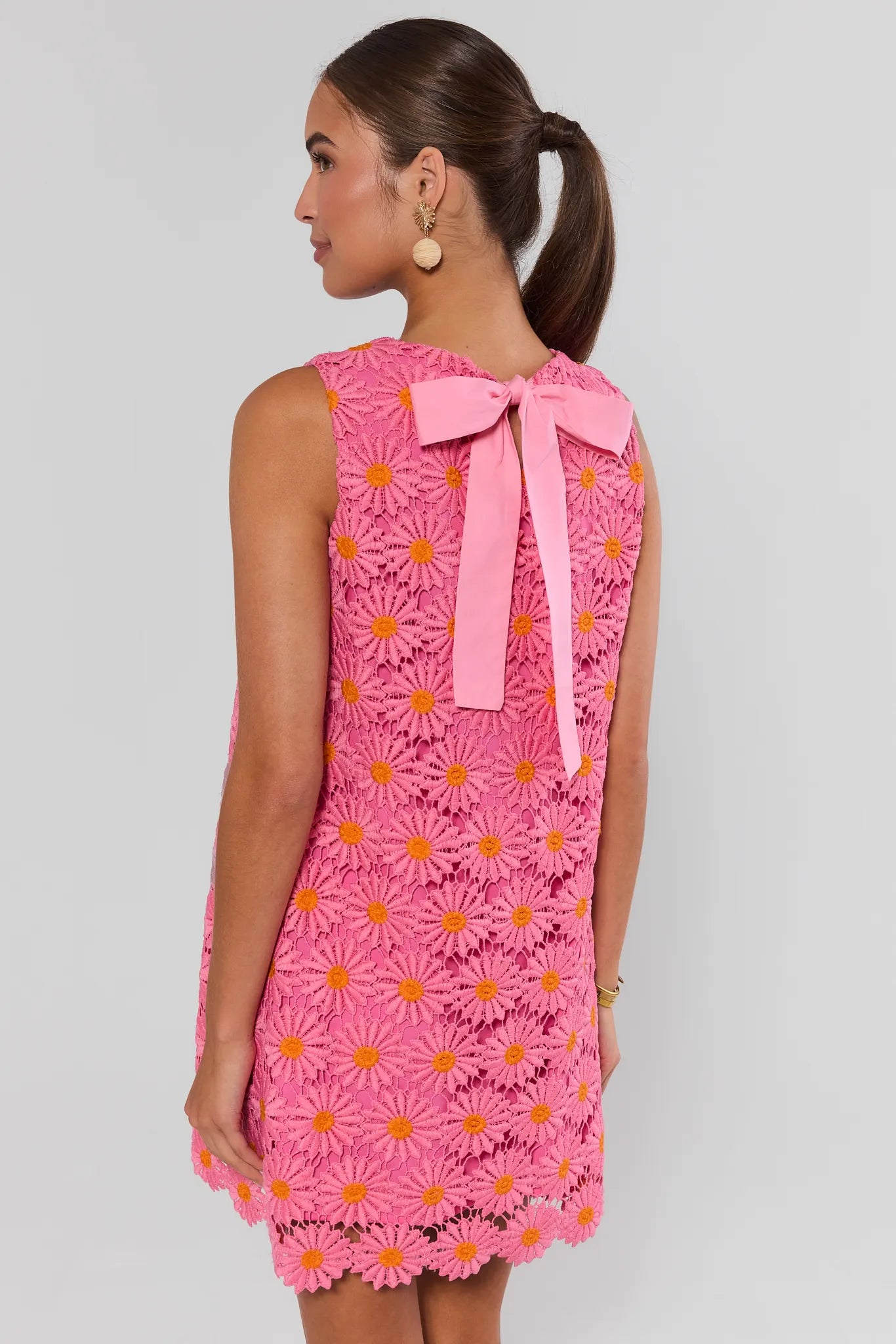 Woman wearing a pink floral dress with a bow on a plain background stand