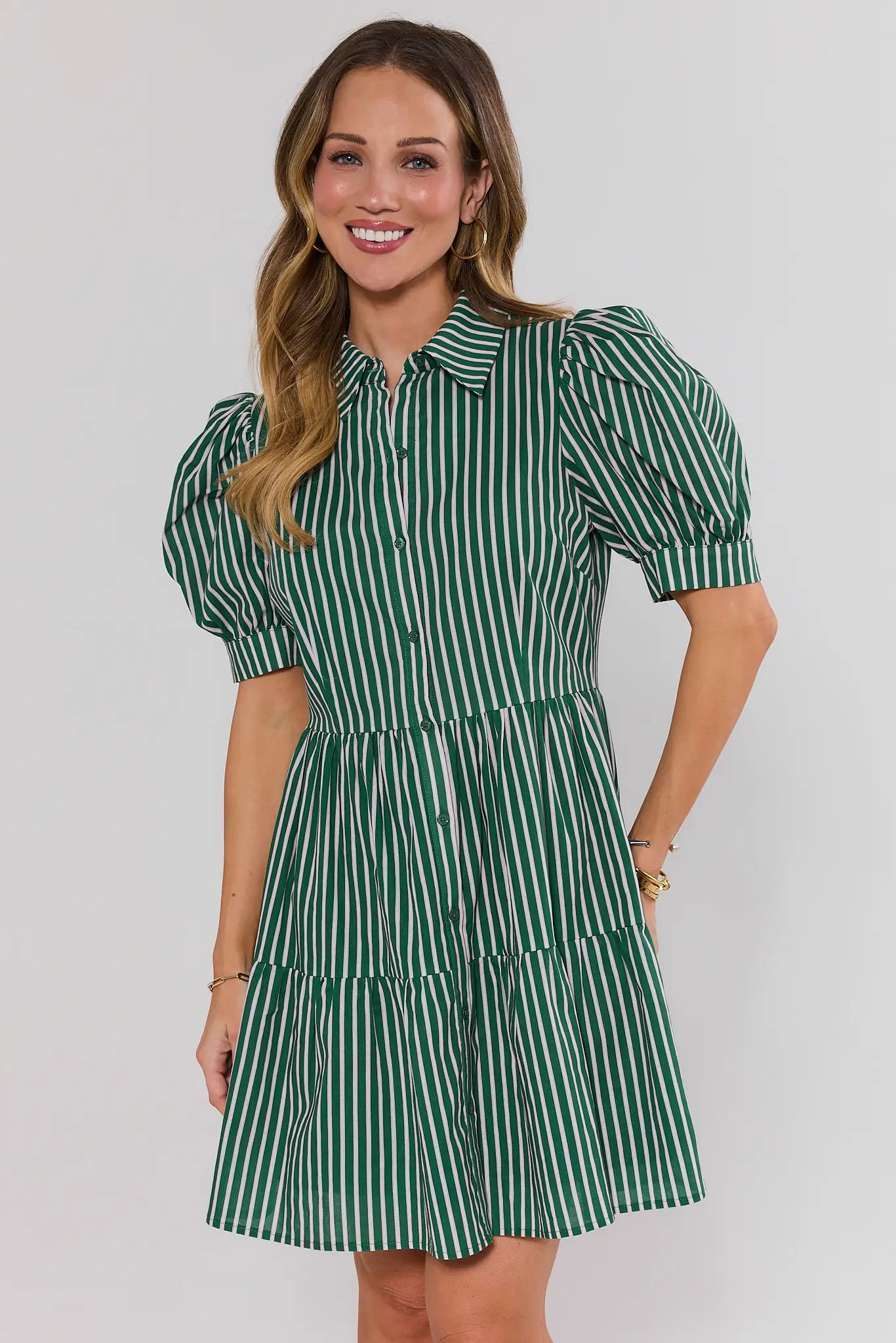 Woman wearing a green and white striped dress against a plain background stand