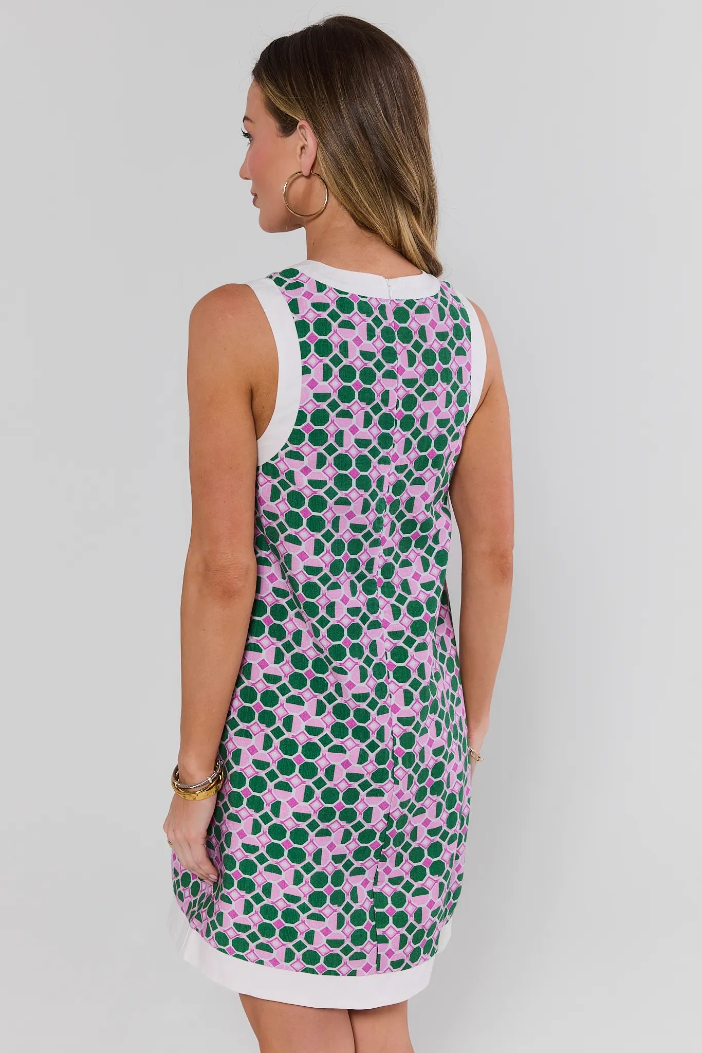 Woman wearing a sleeveless dress with a pink and green pattern on a plain background stand