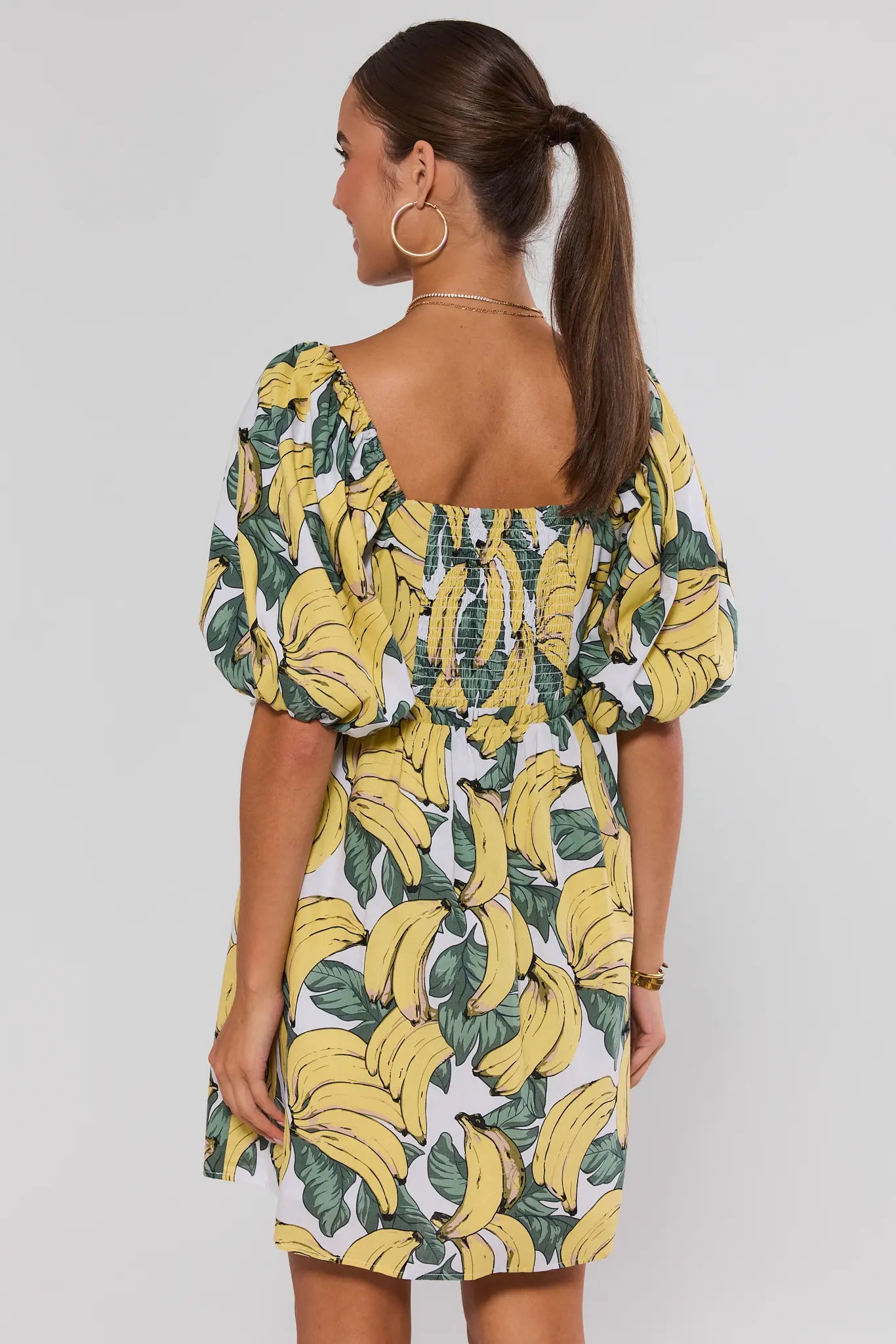 Woman wearing a dress with banana print on a plain background stand