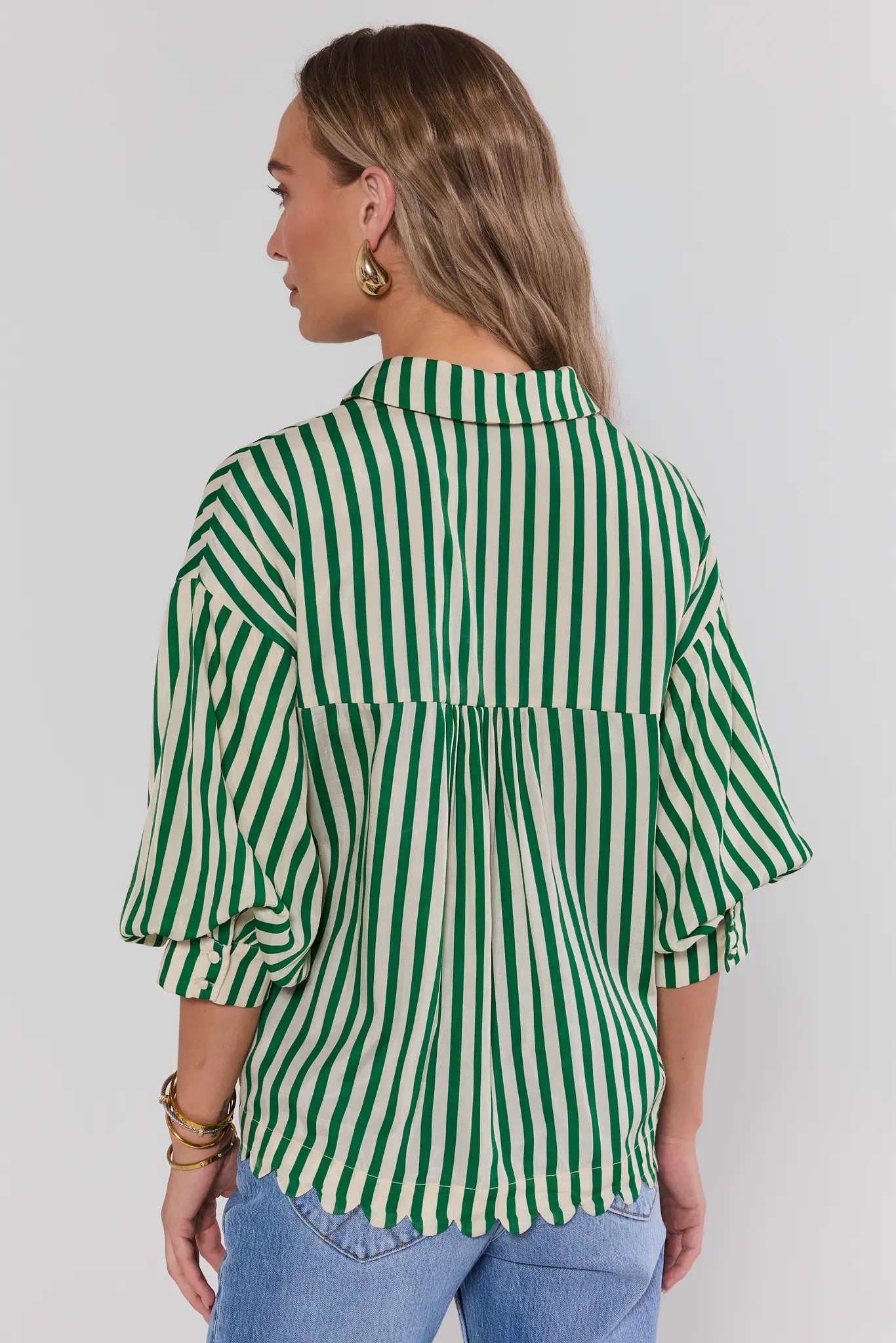 Woman standing wearing a green and white striped shirt against a plain background